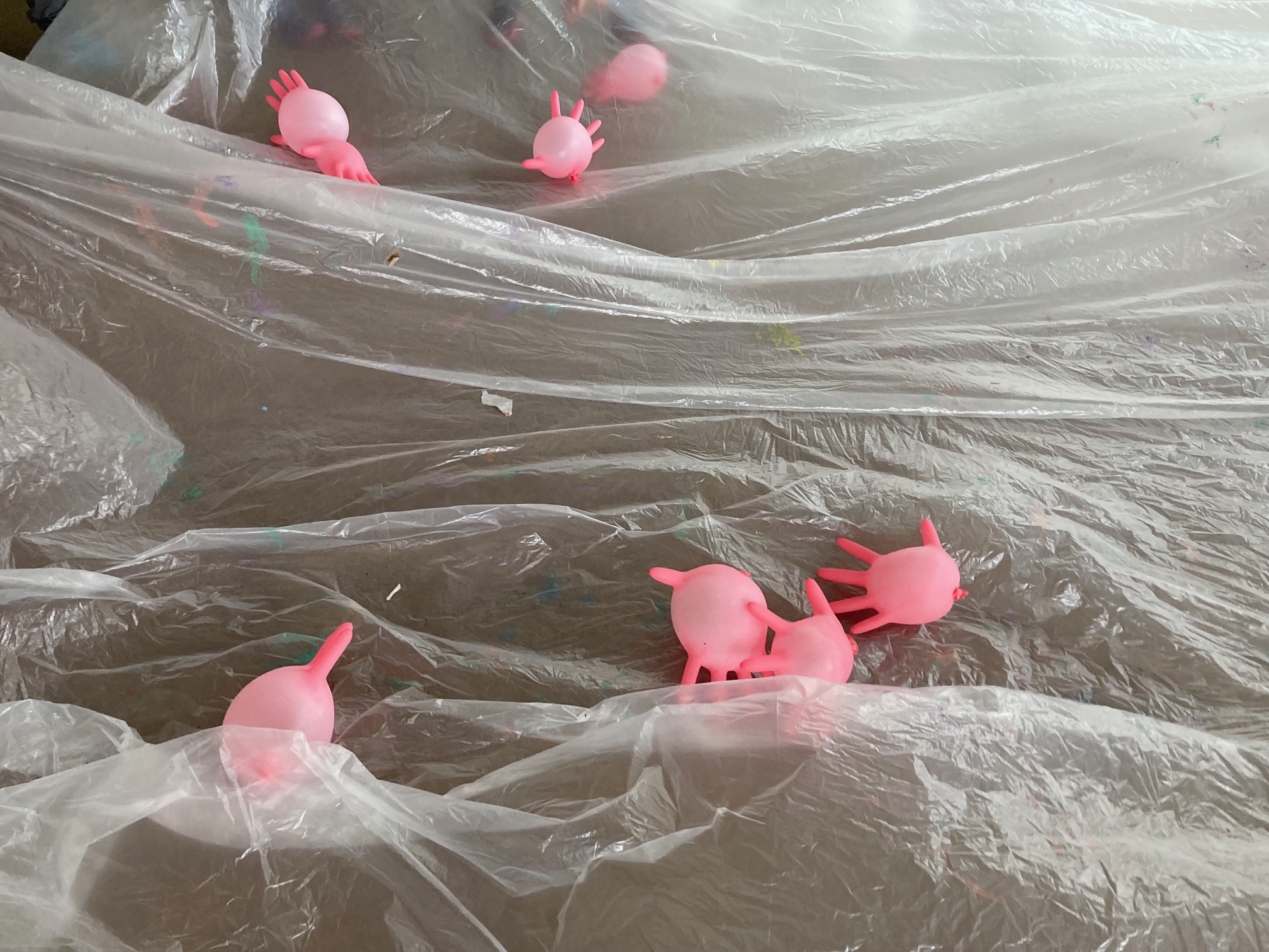 auf einer weißen Folie fliegen aufgeblasene rosa Gummihandschule, die wie Plankton anmuten, herum