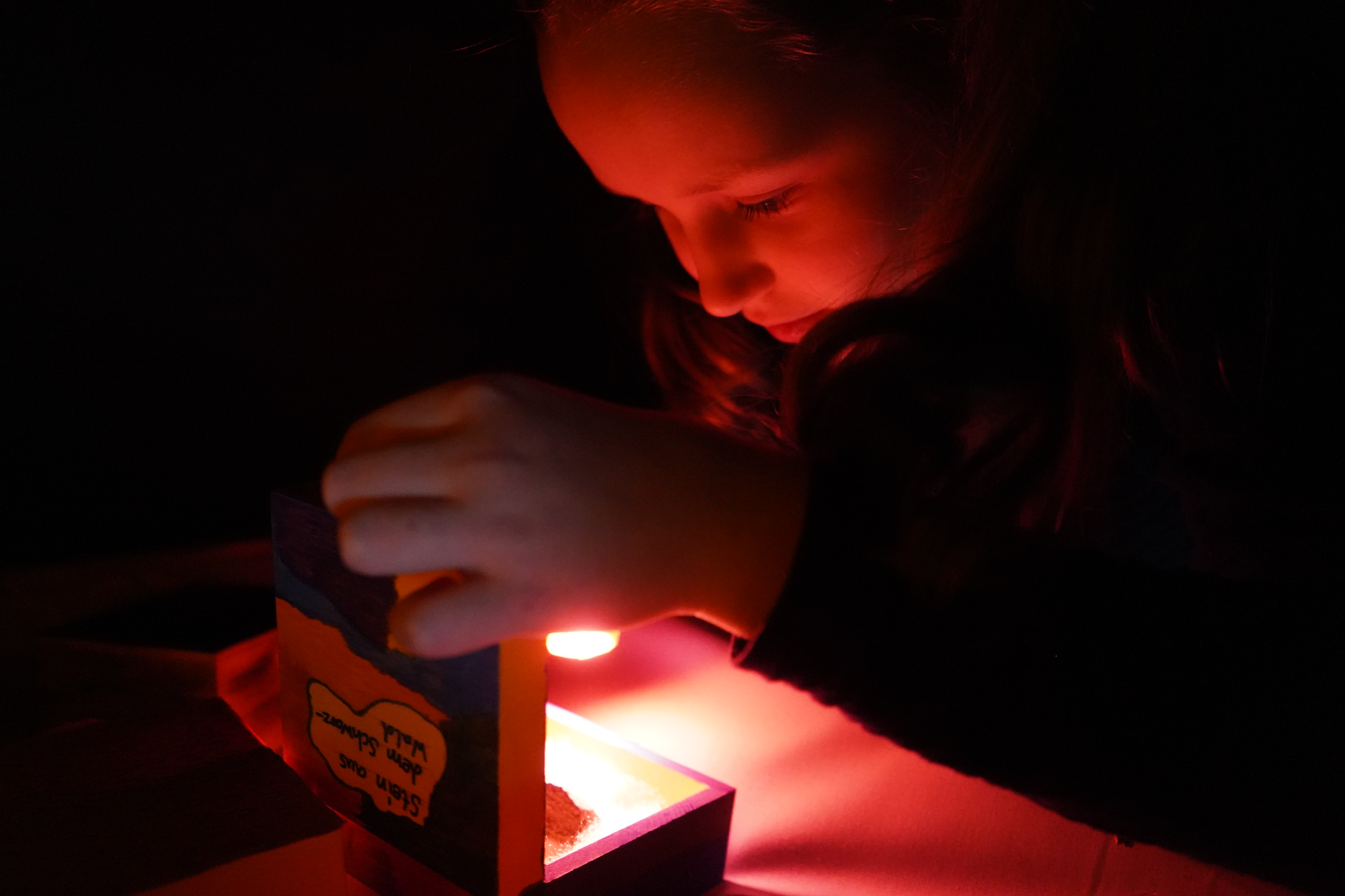 ein Mädchen betrachtet mit einer Taschenlampe den Inhalt eines kleinen Kästchens im dunklen Raum