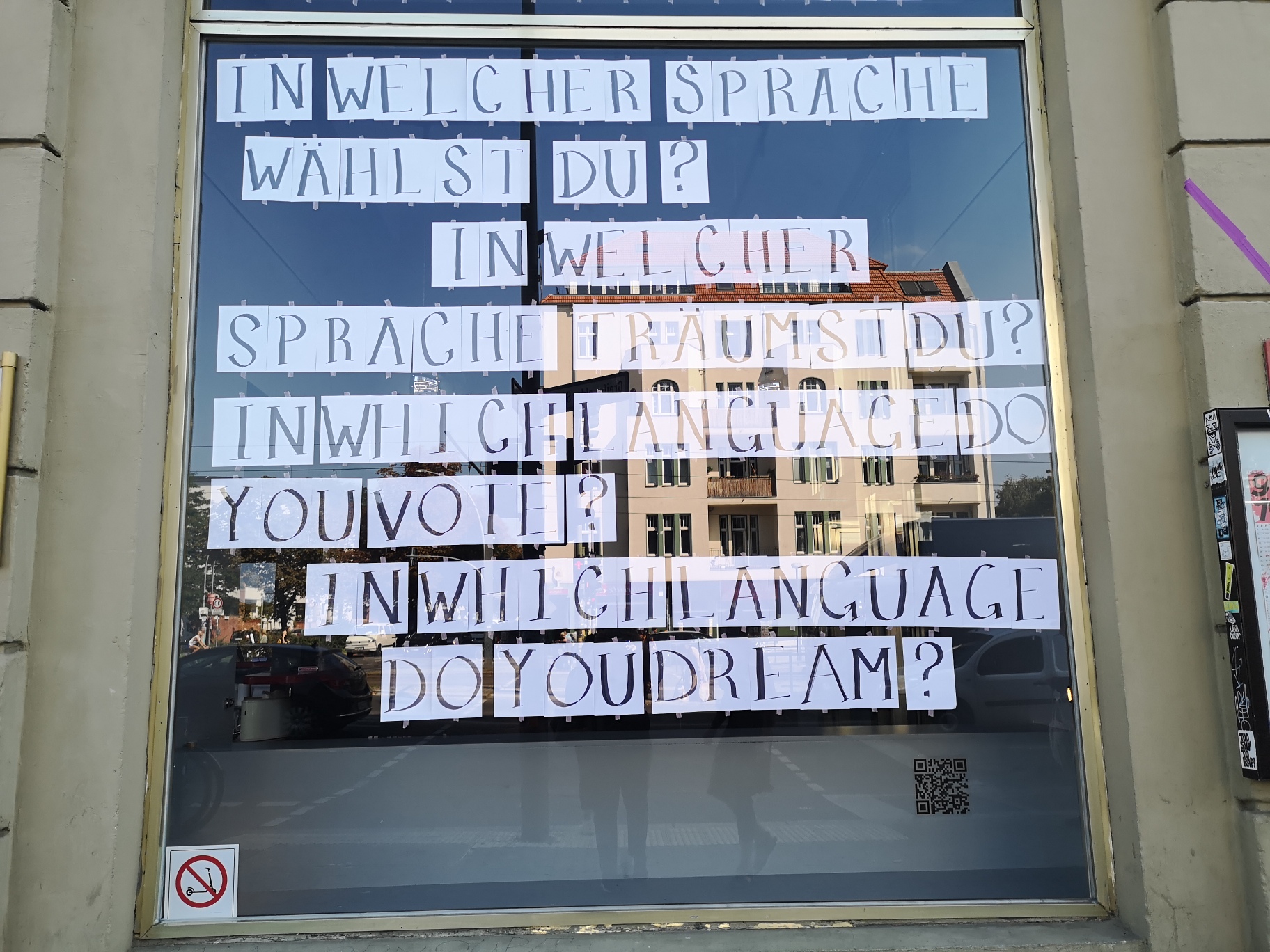 Schaufenster der Schaubude mit auf Din-A4-Zetteln geschriebenen Buchstaben, die zusammen die Fragen ergeben: In welcher Sprache wählst du? In welcher Sprache träumst du?