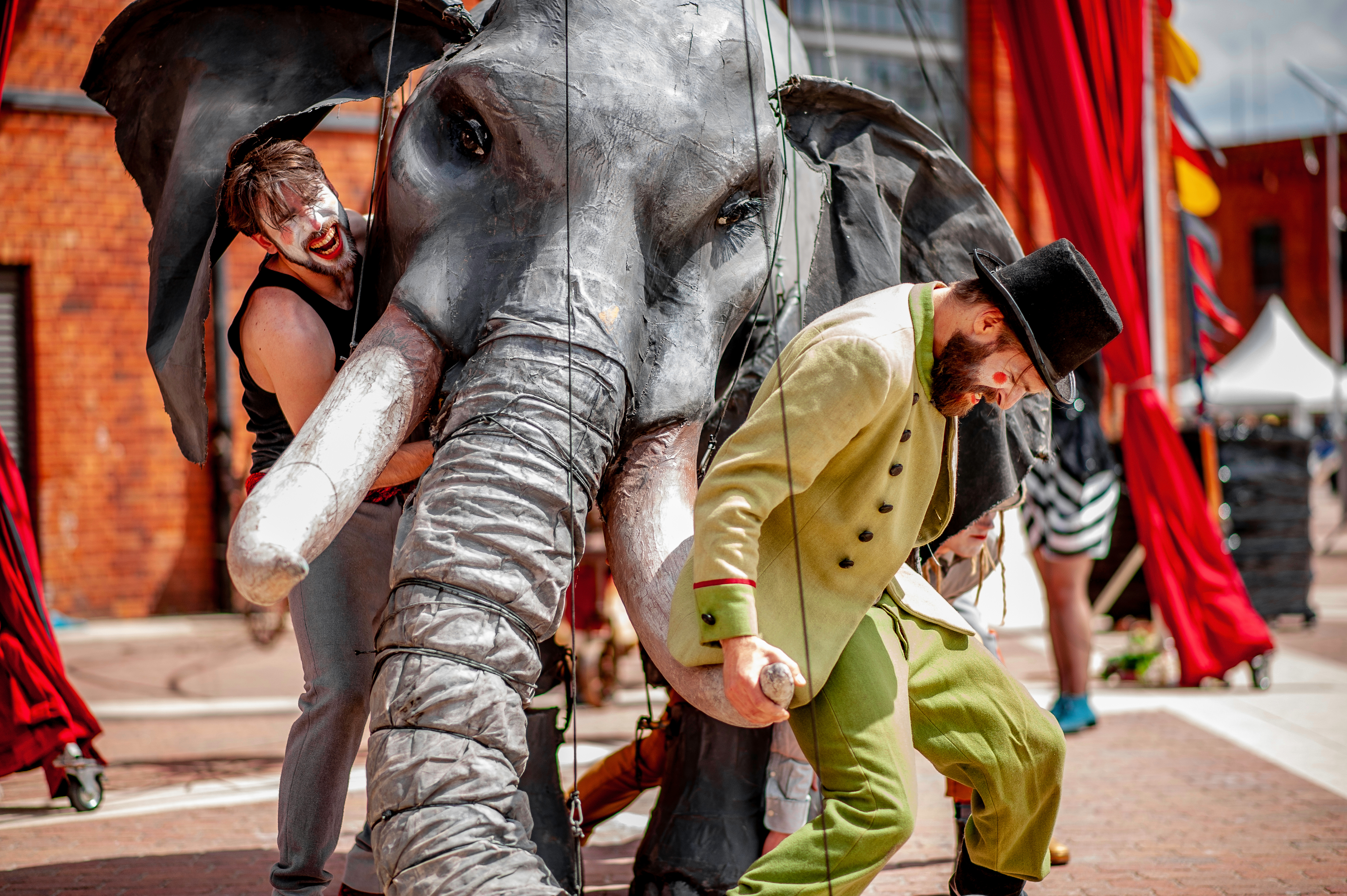 Eine riesige Elefanten-Marionnette wird von zwei Männern in Clownsmasken gestützt.