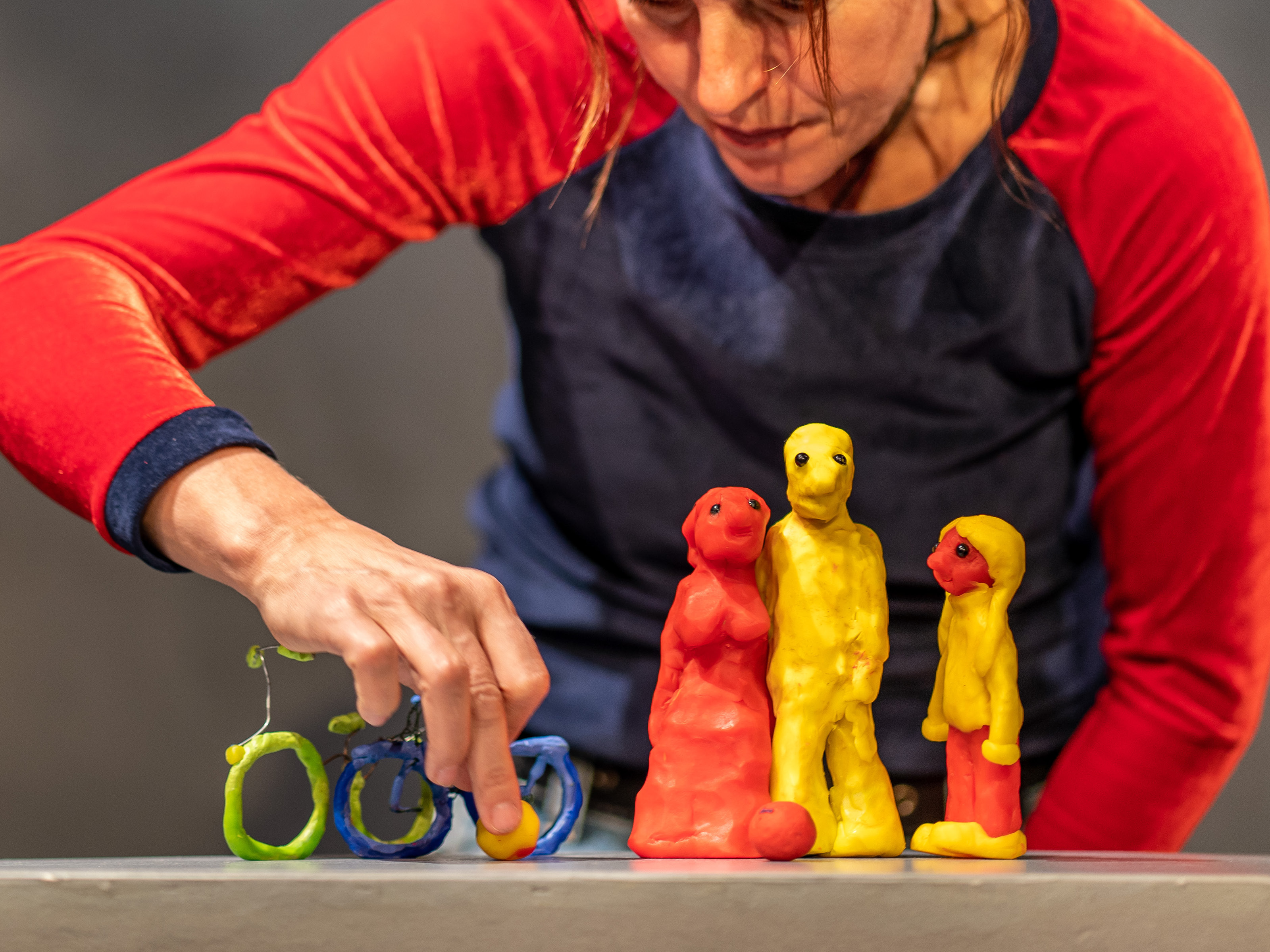 Puppeteer Annegret Geist holds a small bicycle made of plasticine with one hand. Next to the bicycle is a highly abstract three-headed family made of plasticine.