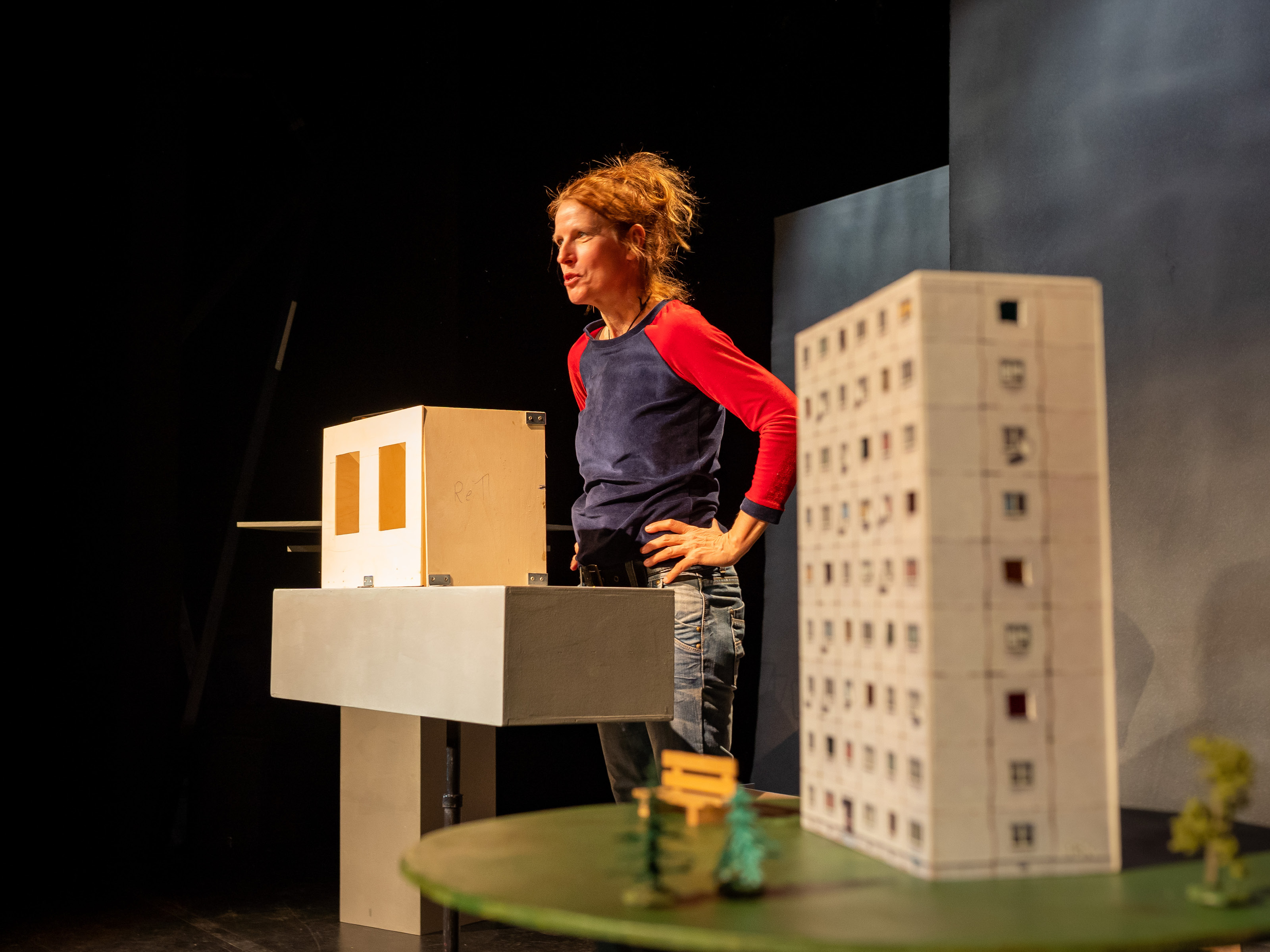 Im Vordergrund des Bildes ist das Modell eines Hochhauses mit neun Stockwerken zu sehen. Im Hintergrund steht Puppenspielerin Annegret Geist mit in die Hüften gestemmten Händen.