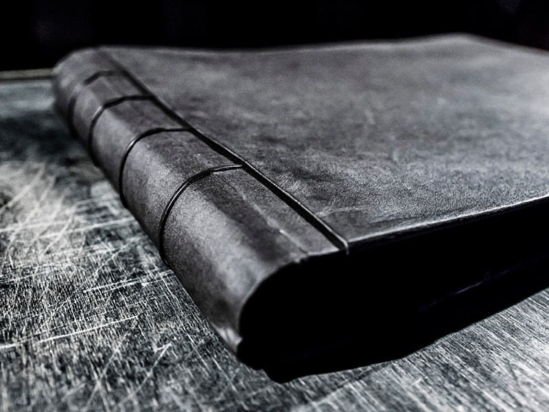 Ein schwarzes, in Leder eingeschlagenes Buch auf einem schwarzen Tisch.