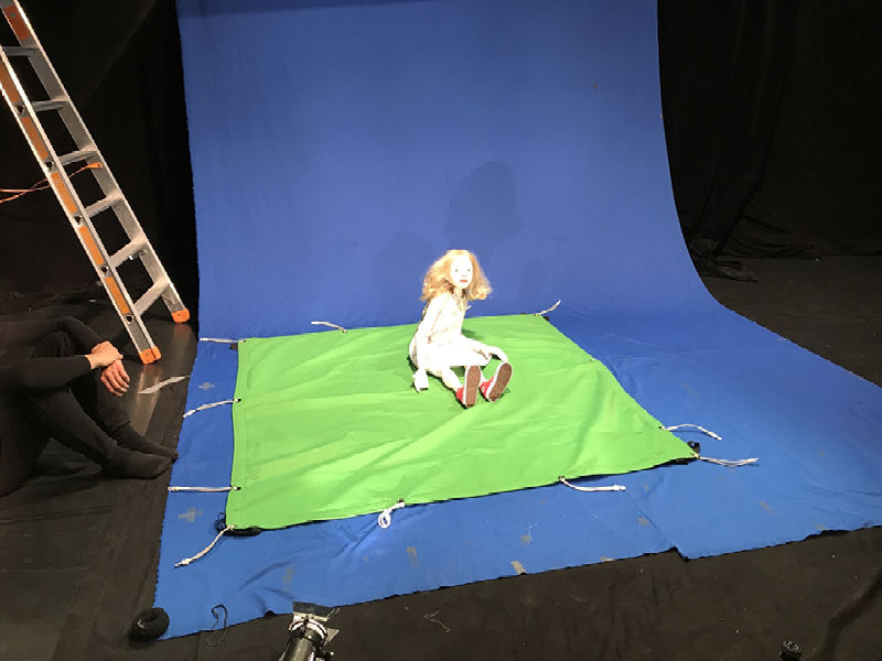ALICE-Puppe auf blauem und grünem Foto-Hintergrundbild sitzend.