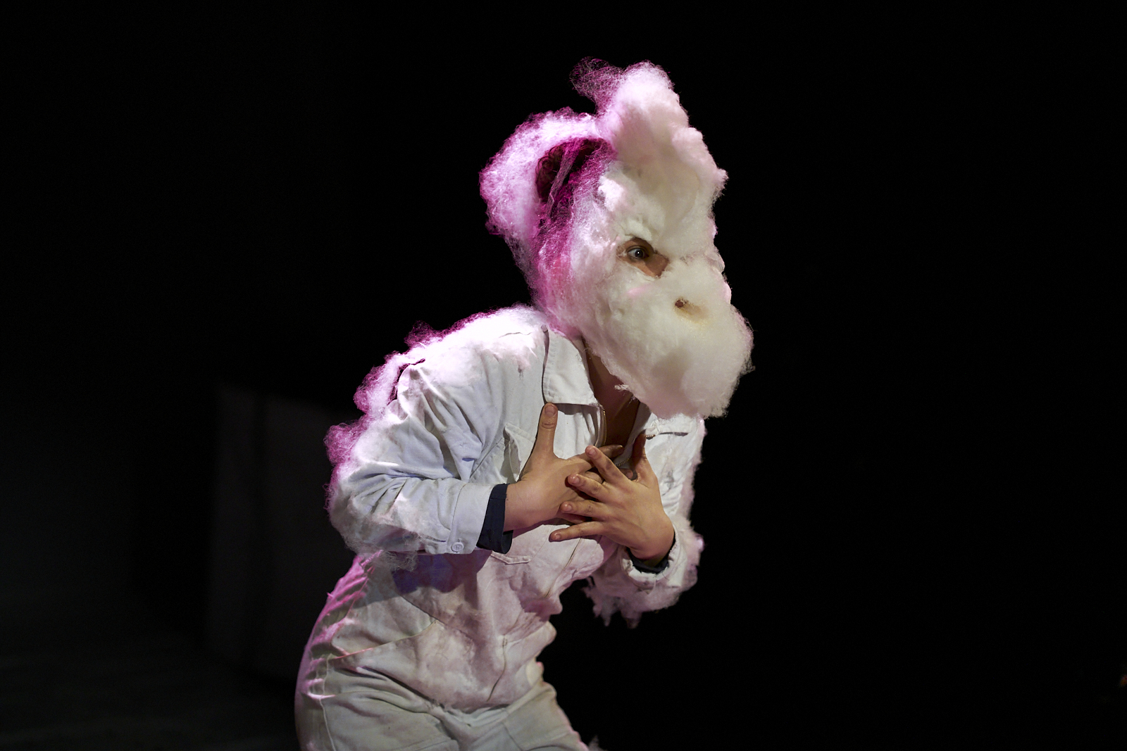 Performerin im weißen Ganzkörperanzug mit einer Maske aus Zuckerwatte, die wie eine Ziege aussieht.