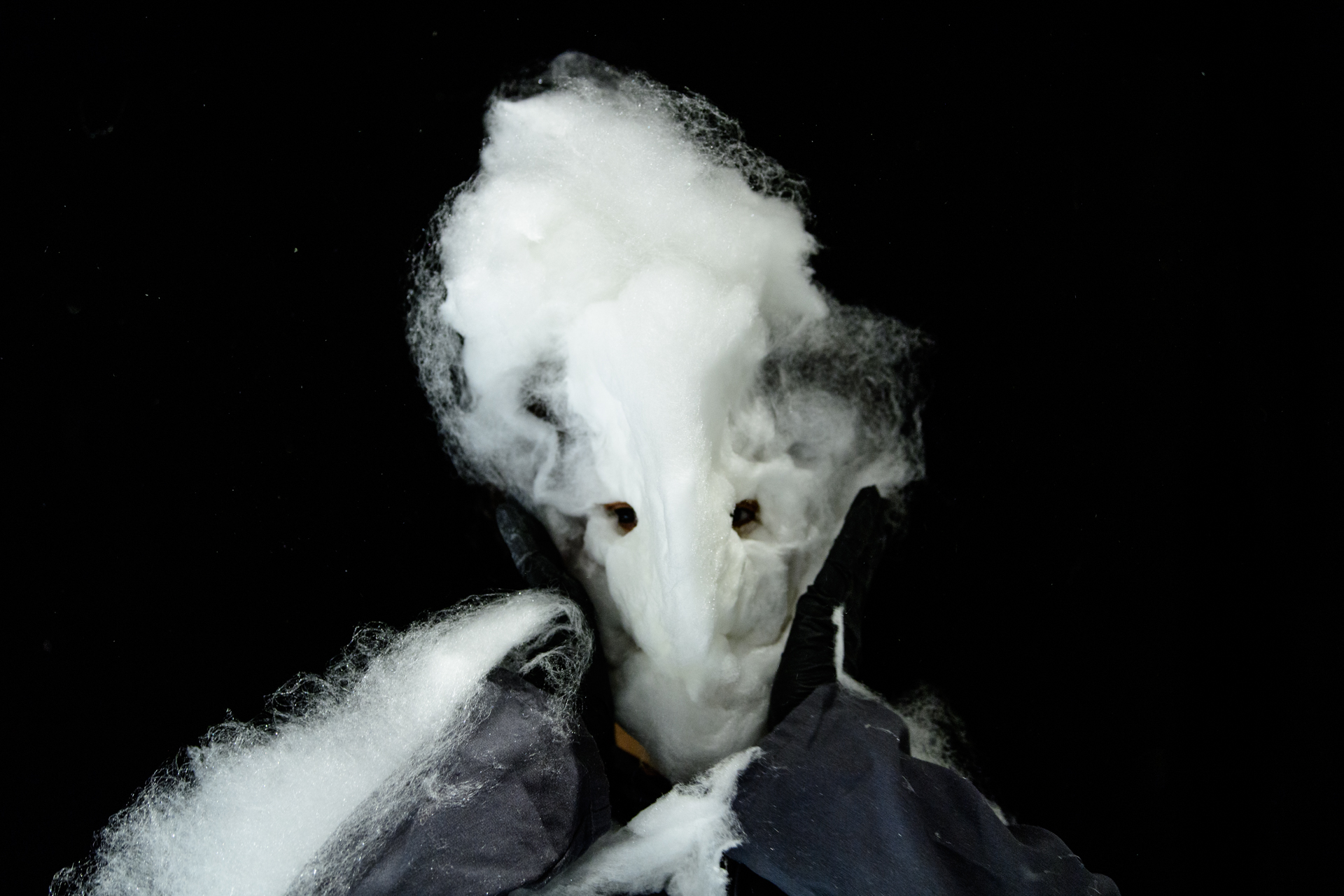 Performerin mit angedeuteter Maske aus Zuckerwatte vor dunklem Bühnenhintergrund.