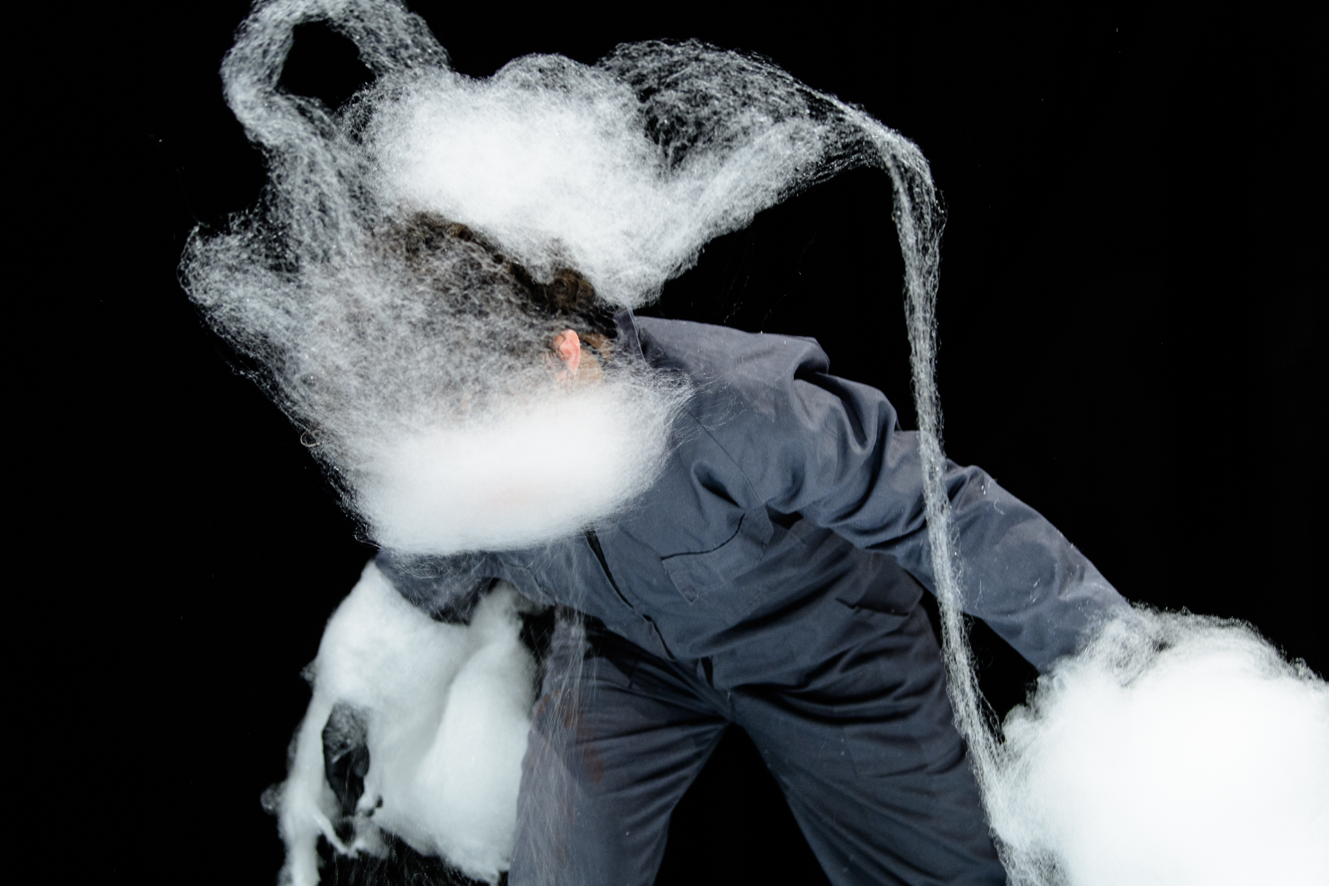 Einer Performerin weht weiße Zuckerwatte ins Gesicht, so dass sich darum eine wolkige Form bildet.