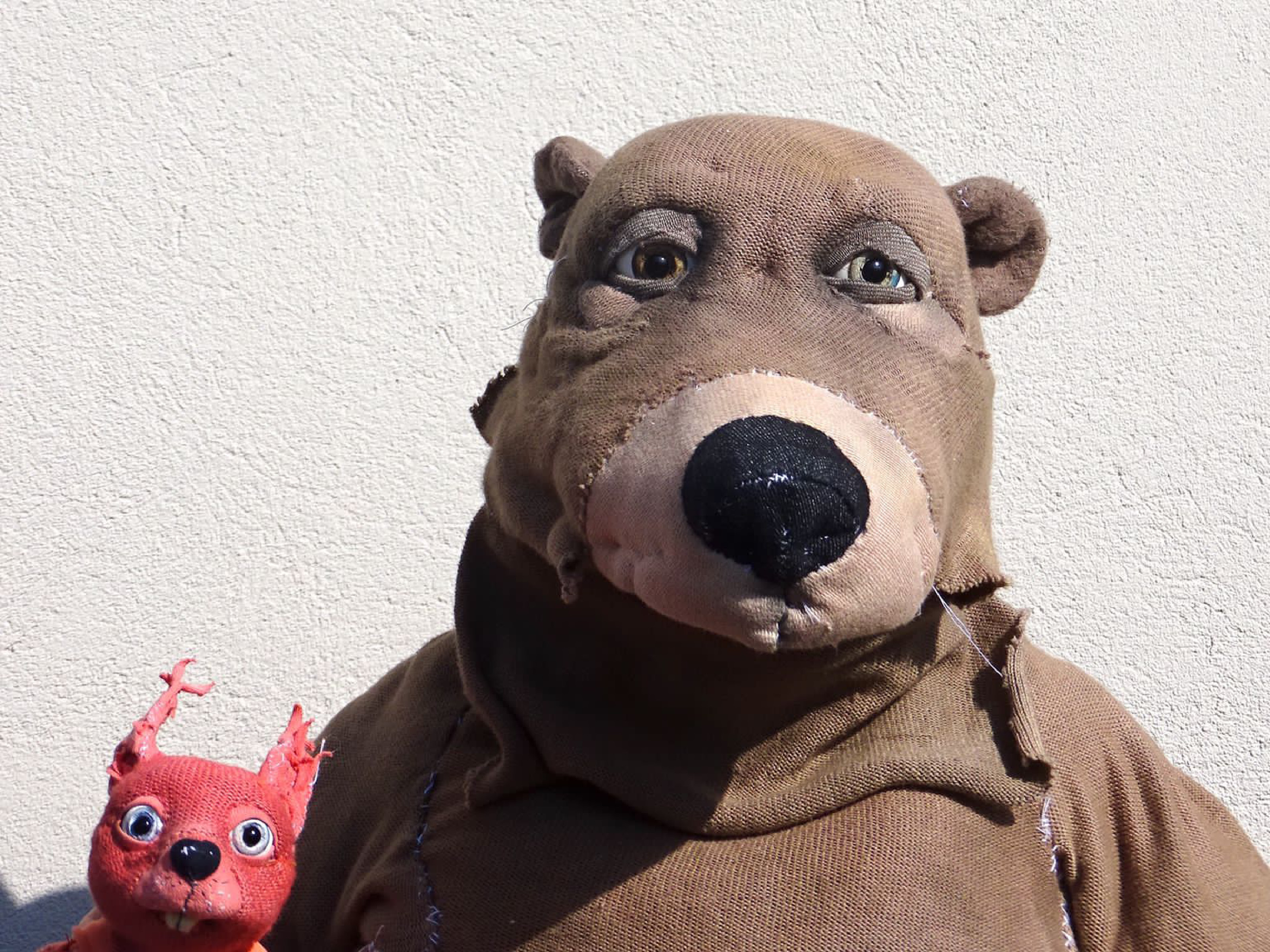 The puppets of a bear and a squirrel can be seen up to the shoulders. They look curiously into the camera.