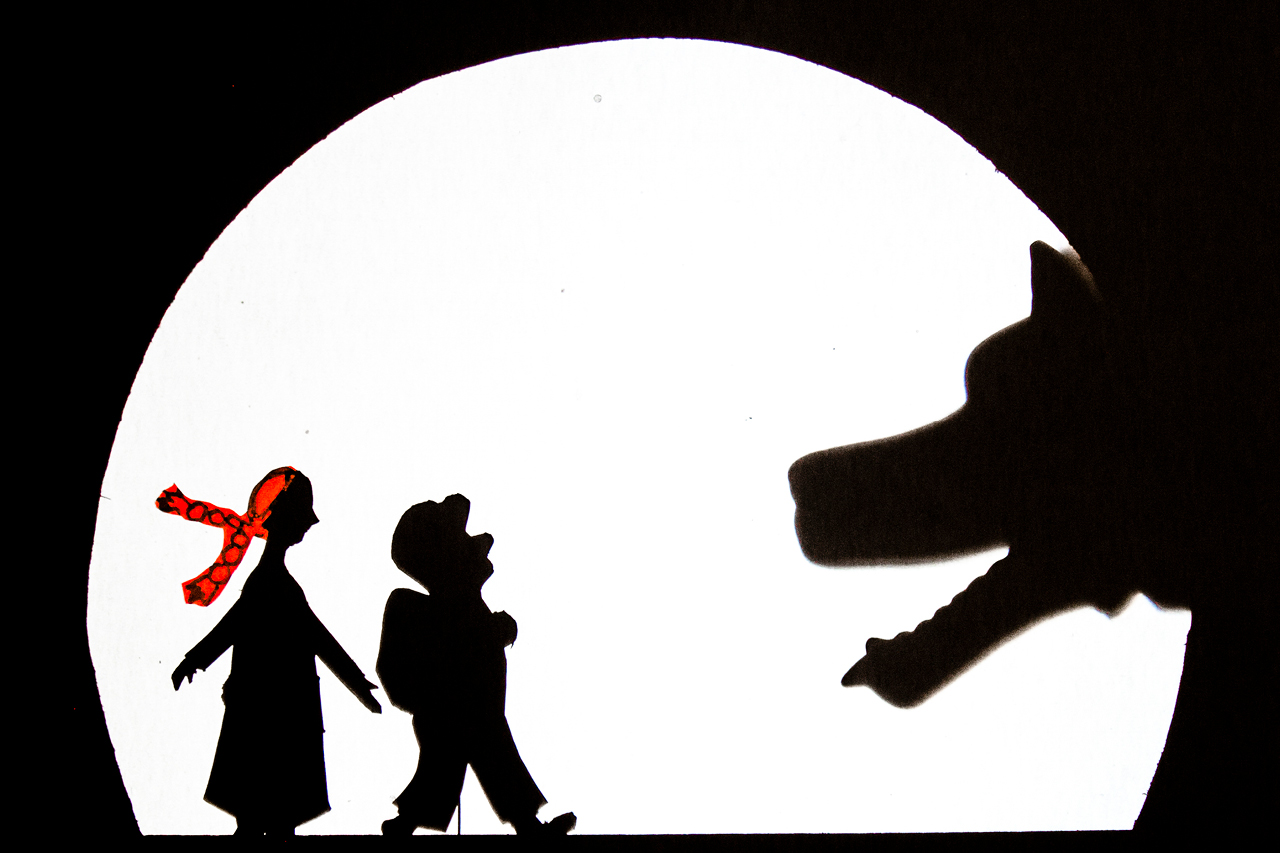 Schattenriss eines kleinen Jungen und eines Mädchens, rechts schaut das Profil eines Wolfskopfs hervor