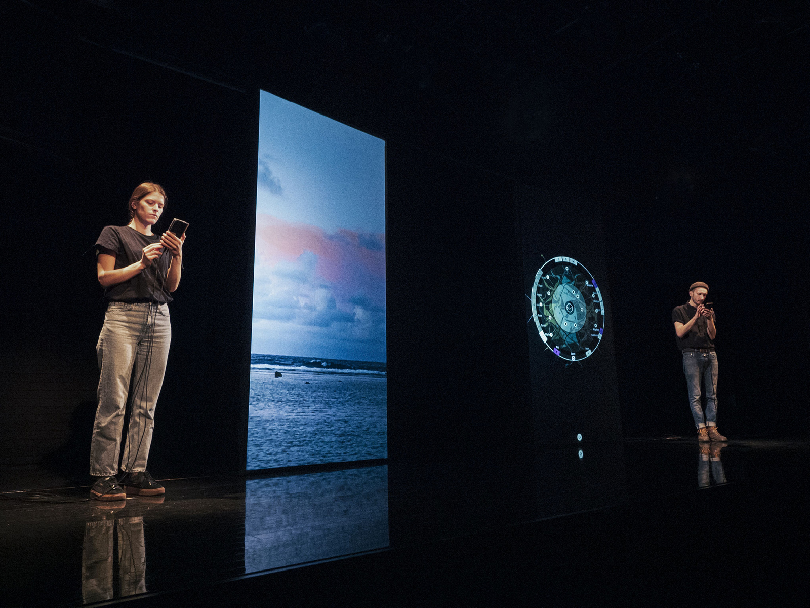 Zwei Leute auf der Bühne, in der Mitte eine Projektionsfläche für Videos.