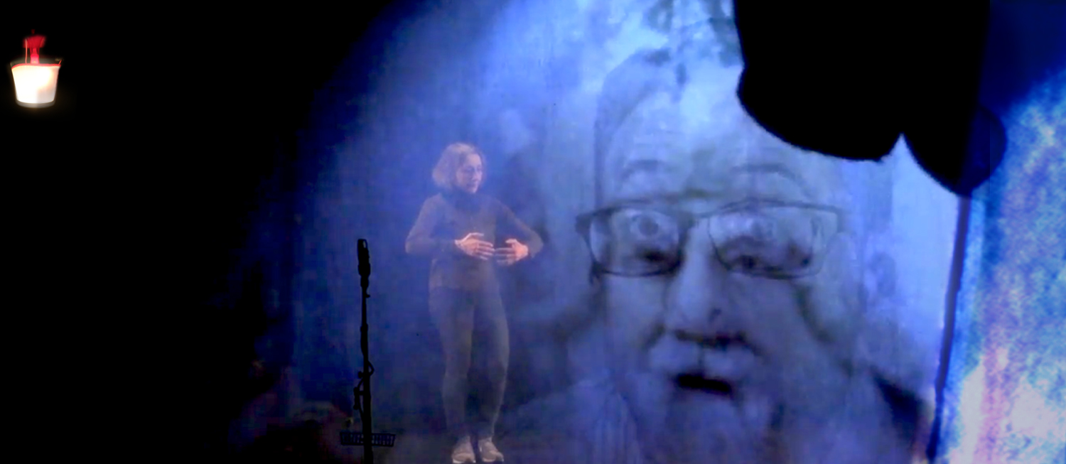 Video-Projektionsfläche zeigt einen alten Mann, dahinter isteht eine Schauspielerin
