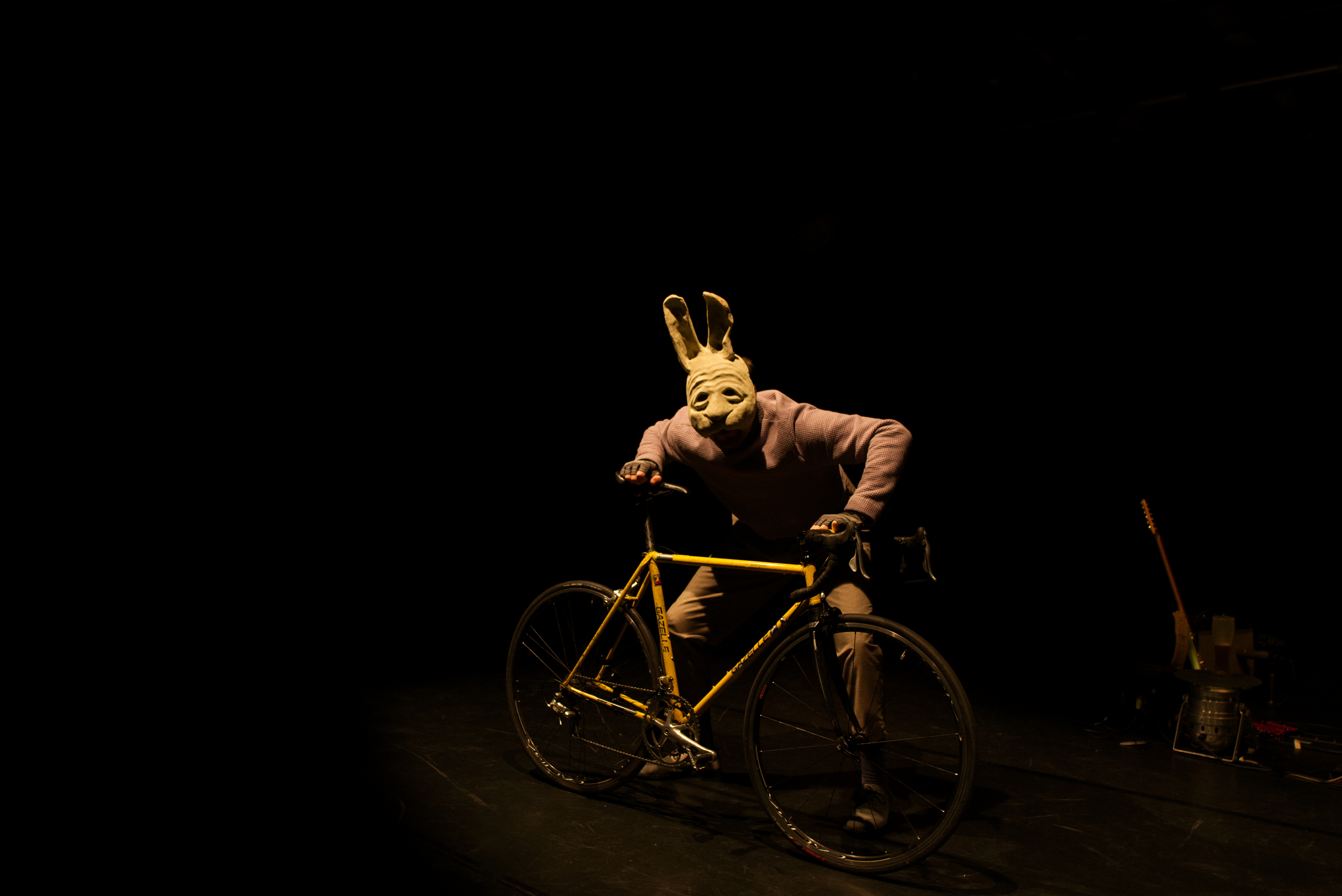 Spieler mit Hasenmaske und Fahrrad in dunklem Bühnenraum