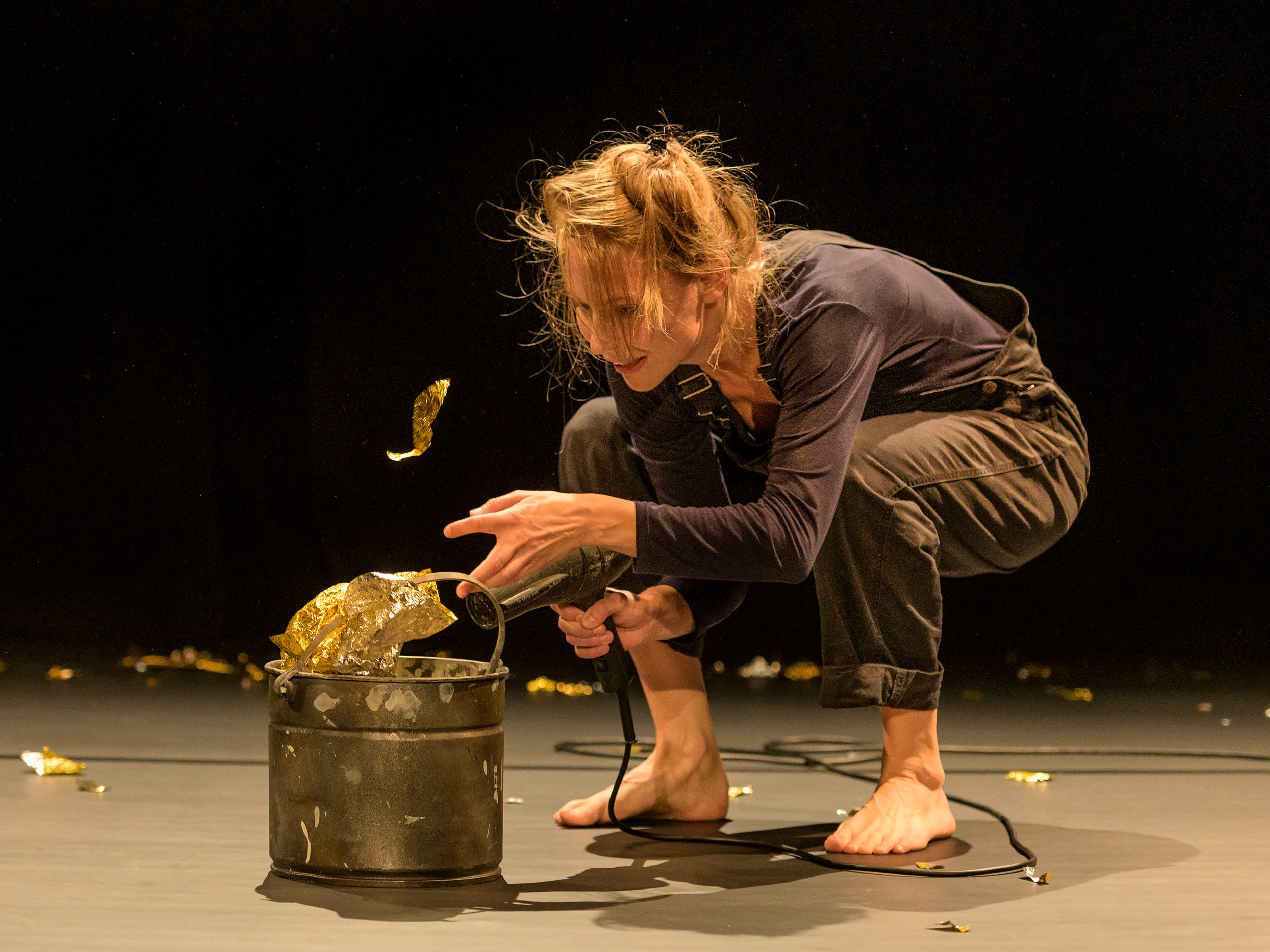 Karoline Hoffmann blows large and small pieces of gold foil out of a metal bucket with a hair dryer.
