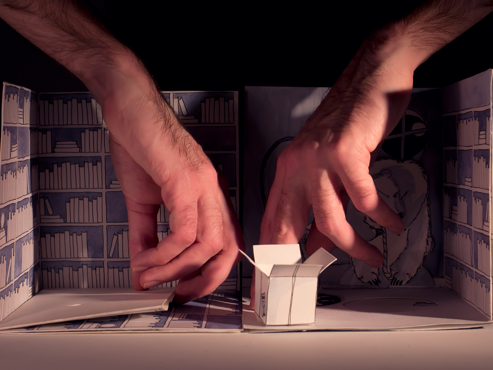 Hände in einer Miniaturbühne, im Vordergrund eine offene Box aus Papier.