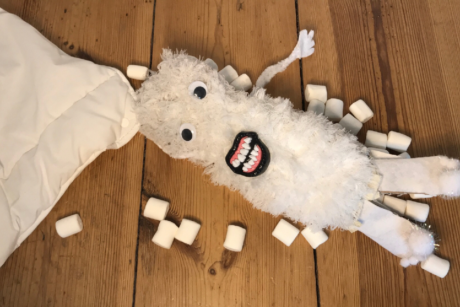 Ein kuscheliges weißes Monster auf einem Dielenboden, daneben Zuckerwürfel.