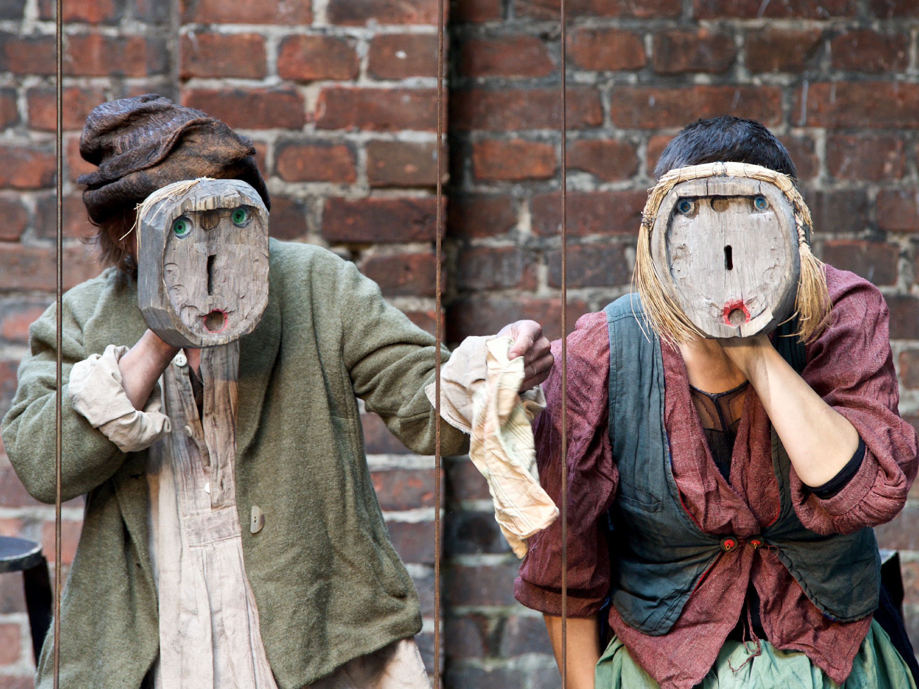Die Spielenden von Hänsel und Gretel halten sich Holzstücke mit minimalistisch angedeuteten Gesichtern vor ihre Gesichter.