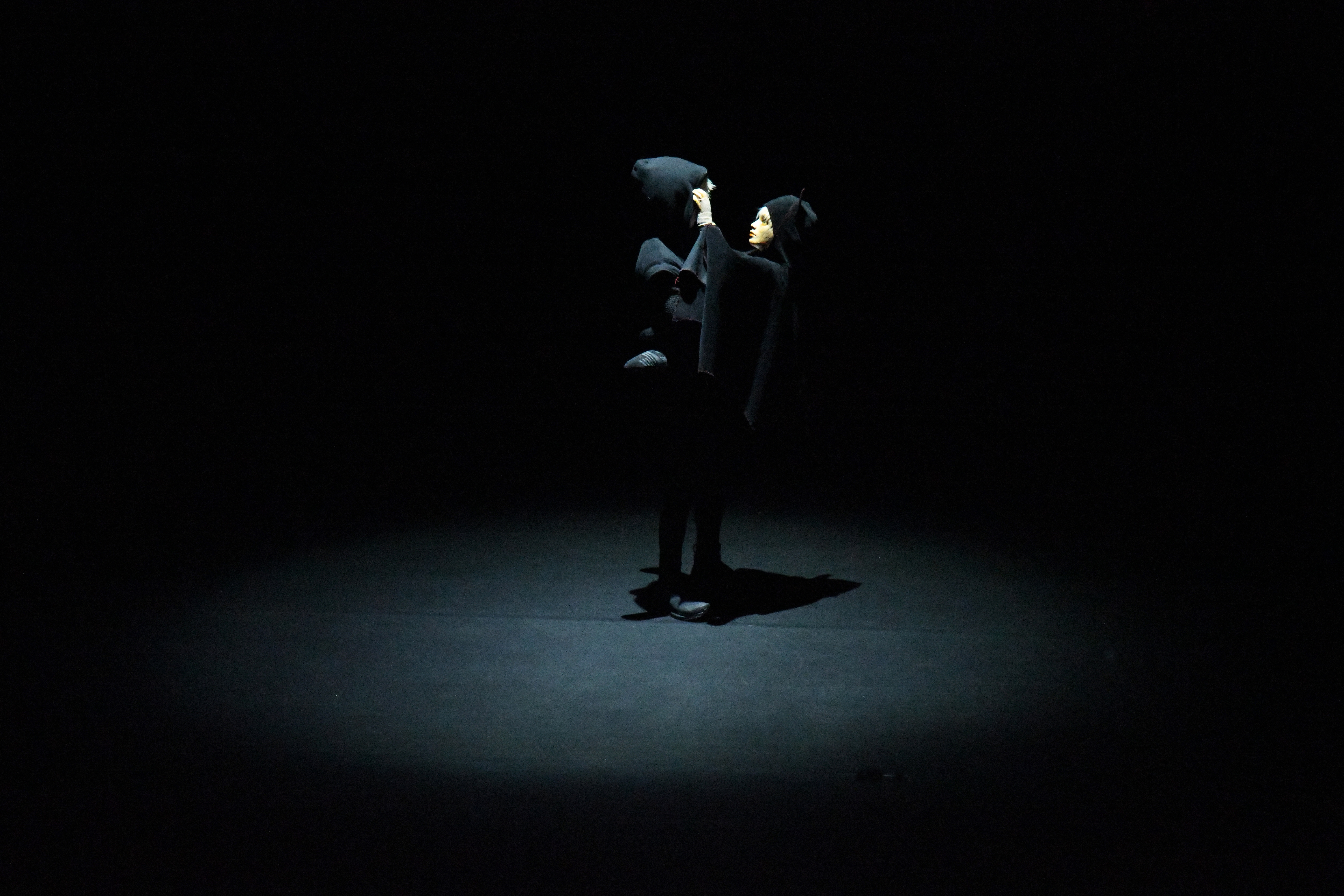 Spieler und Puppe sehen sich ins Gesicht im dunklen Bühnenraum.