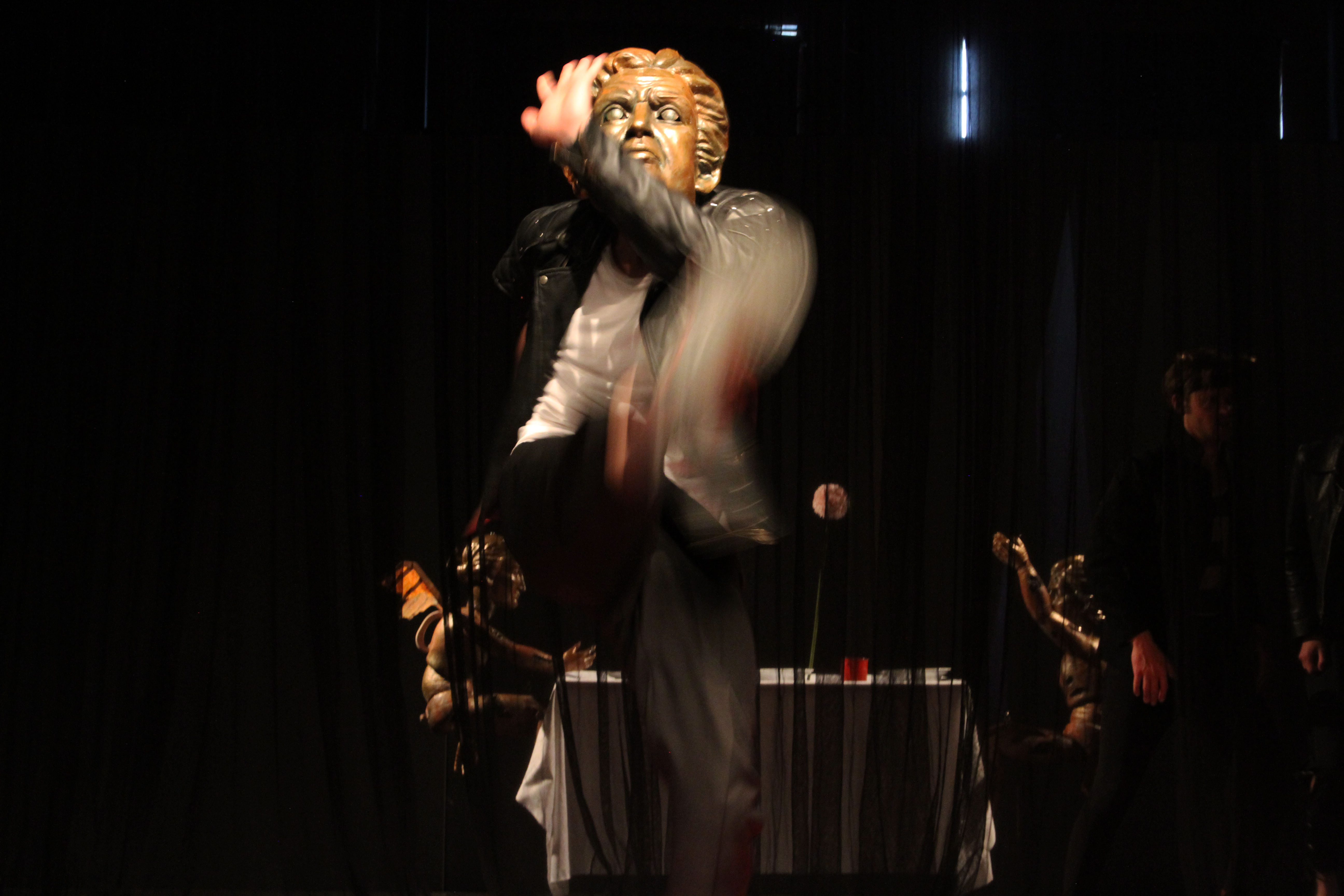A man with an antique golden face mask steps towards the camera. His movements are blurred.