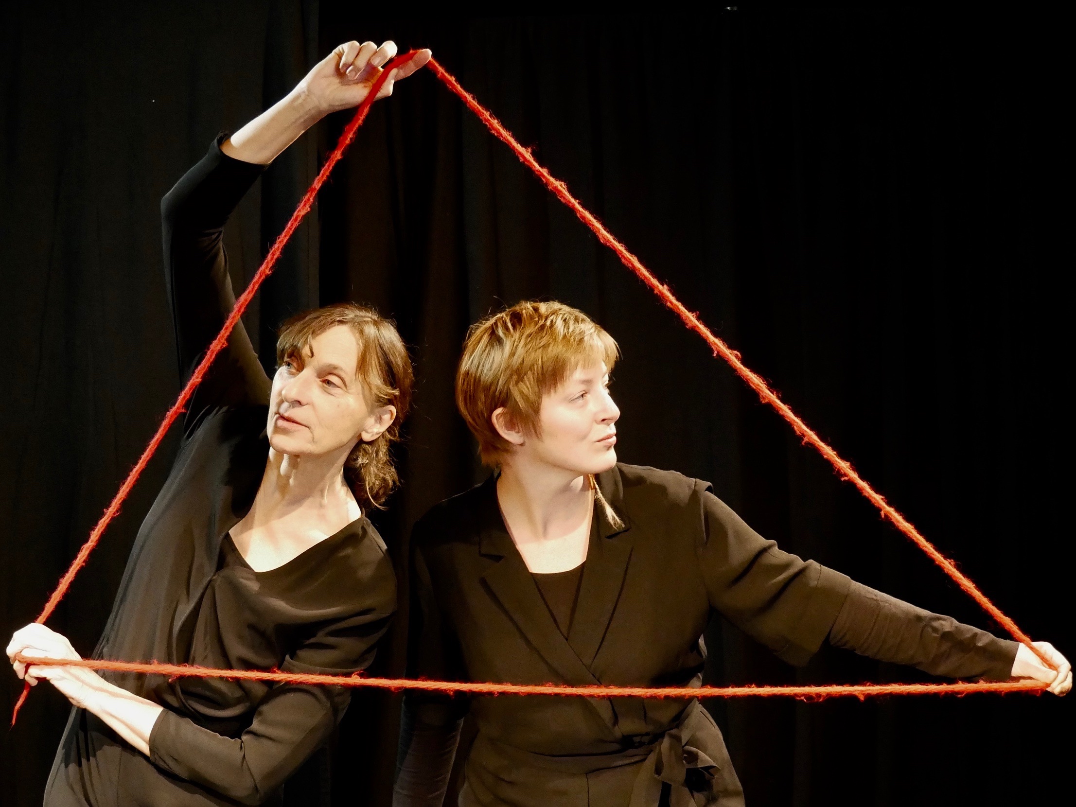 Zwei Spielerinnen, die einen dicken roten Faden wie ein Dreieck formen und um sich herum halten.
