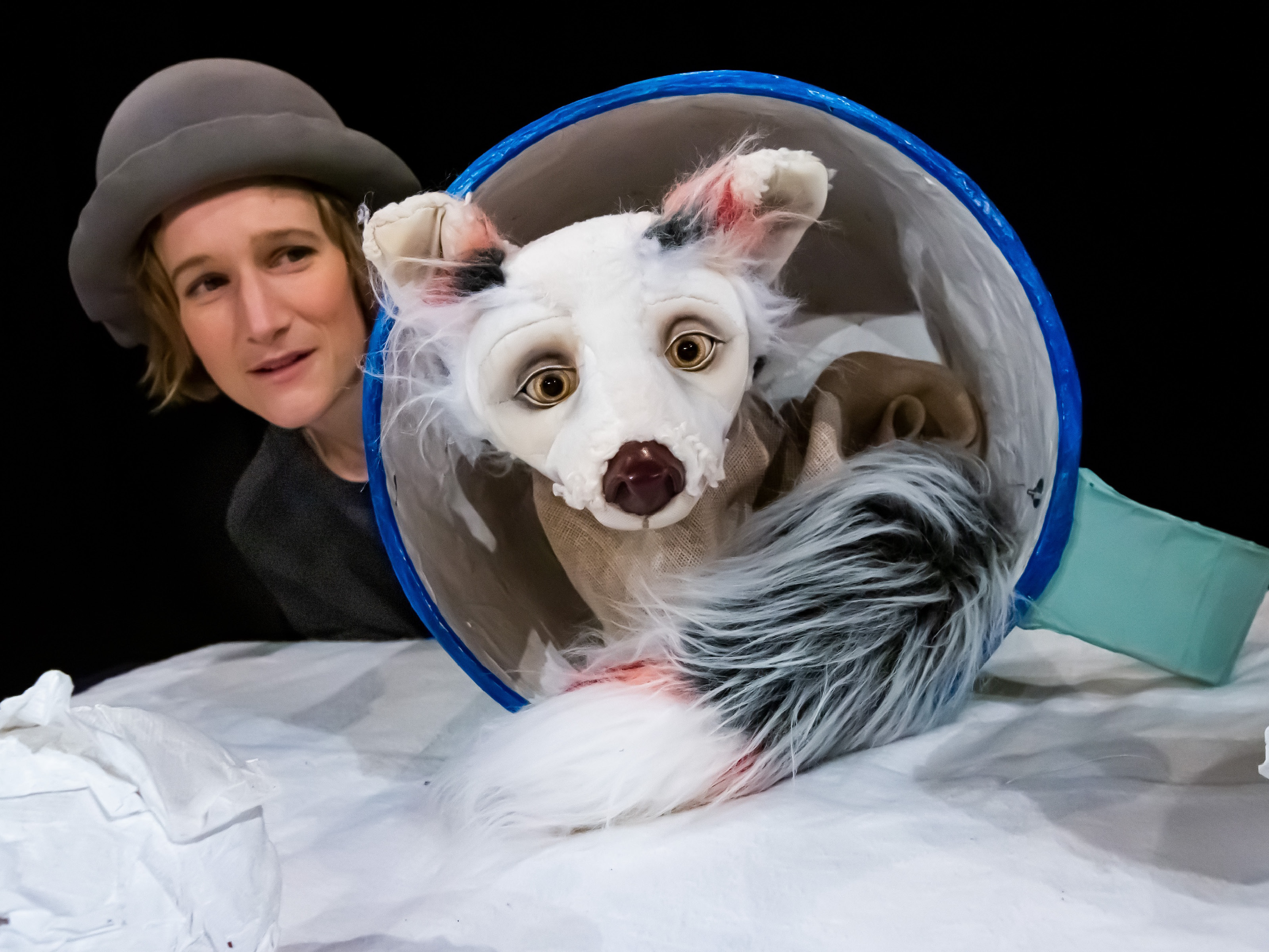 The doll figure of an arctic fox sits curled up in a giant cup. Behind the cup is the player Miriam Hesse. She is wearing a gray hat.