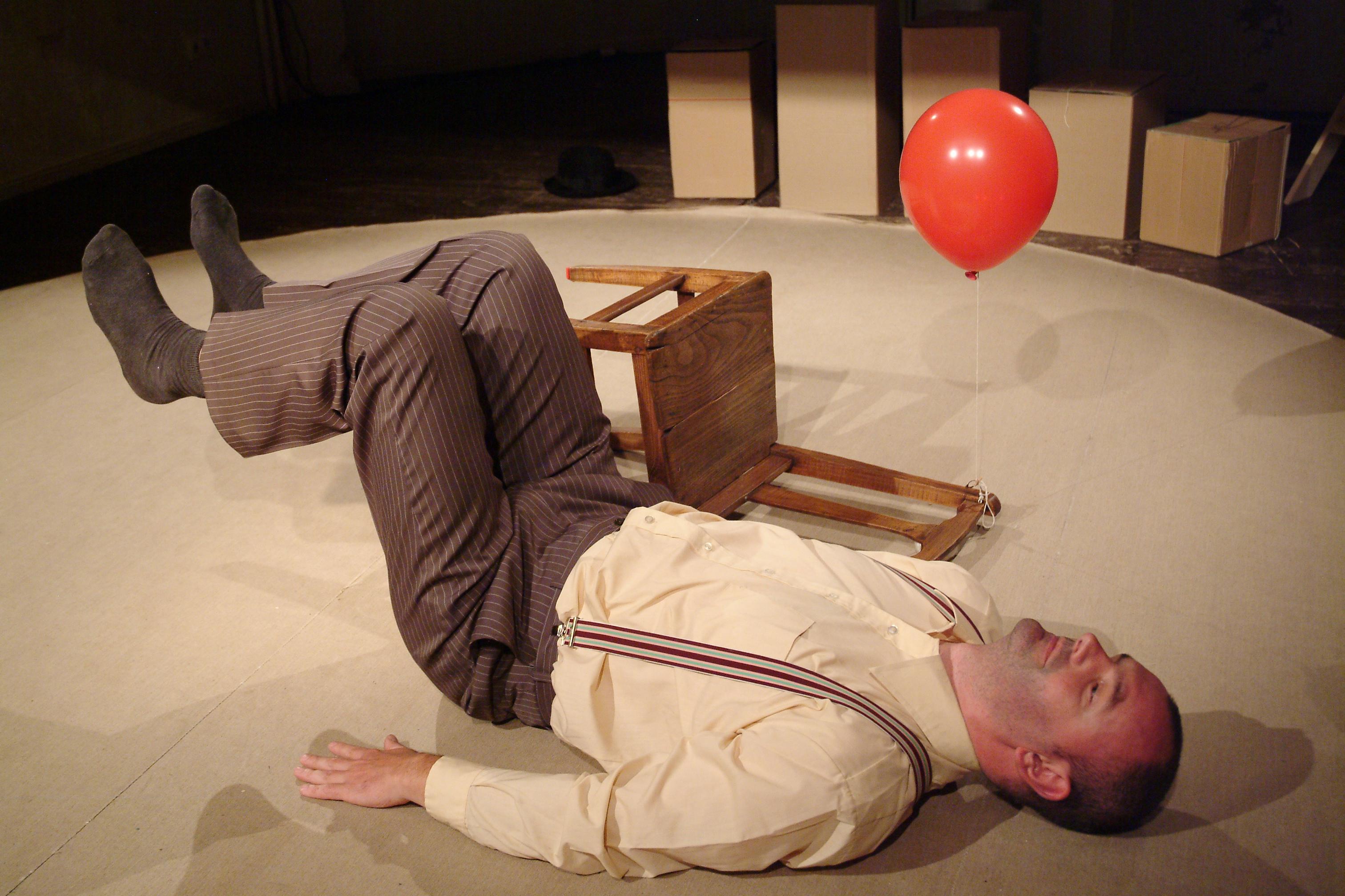 Michael is lying on the floor with his legs bent. Next to him is a chair in the same pose. A flying red balloon hangs from the chair.