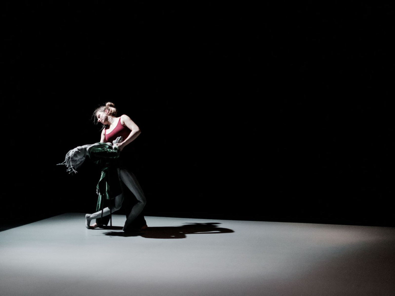 Eine menschgroße, graue Puppe tanzt in einem dunklen Raum mit ihrer Puppenspielerin.