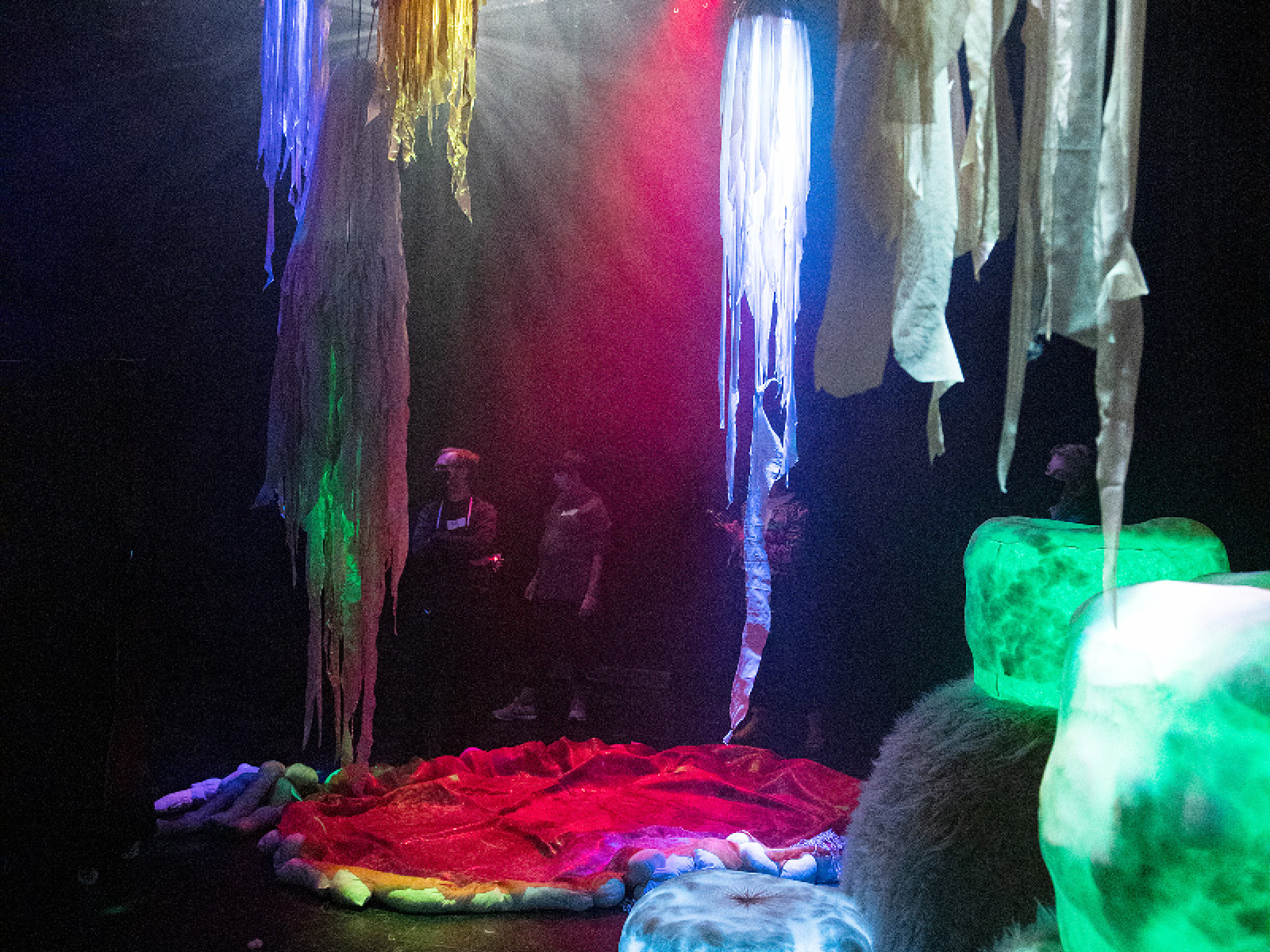 Bühne mit leuchtenden Stoffen und Objekten, im Hintergrund einige Spieler