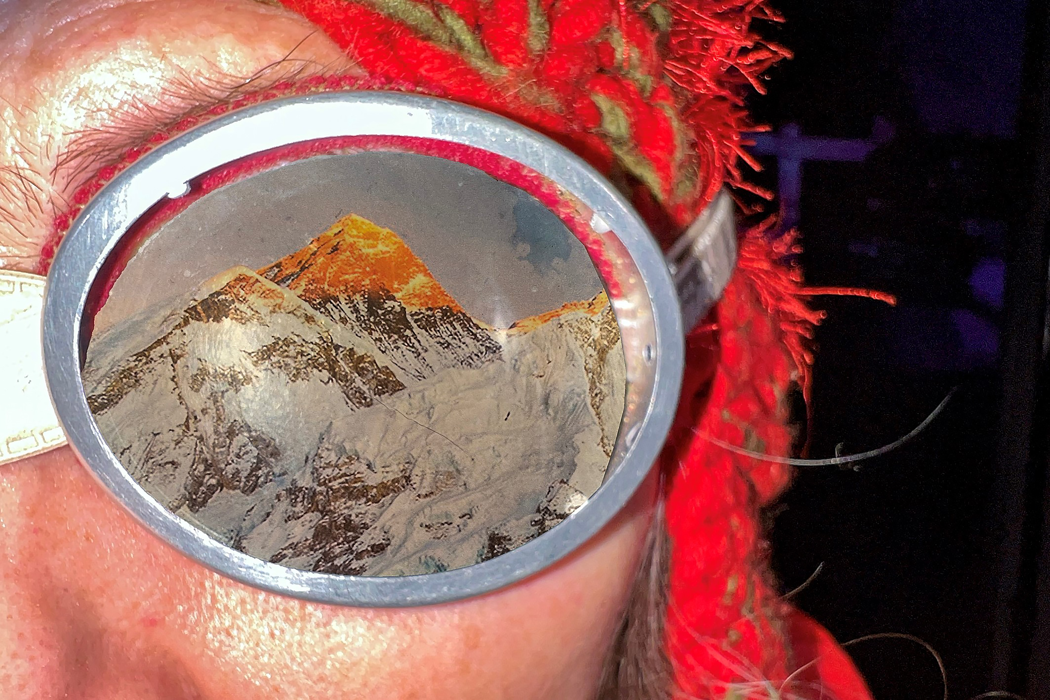 Close-up auf die Sonnenbrille einer der Puppenspielerinnen, in die sich scheinbar der Mount Everest einspiegelt. Bei genauerem Hinsehen erkennt man jedoch, dass die Brille nur mit einer Fotografie des berühmten Berges beklebt ist.