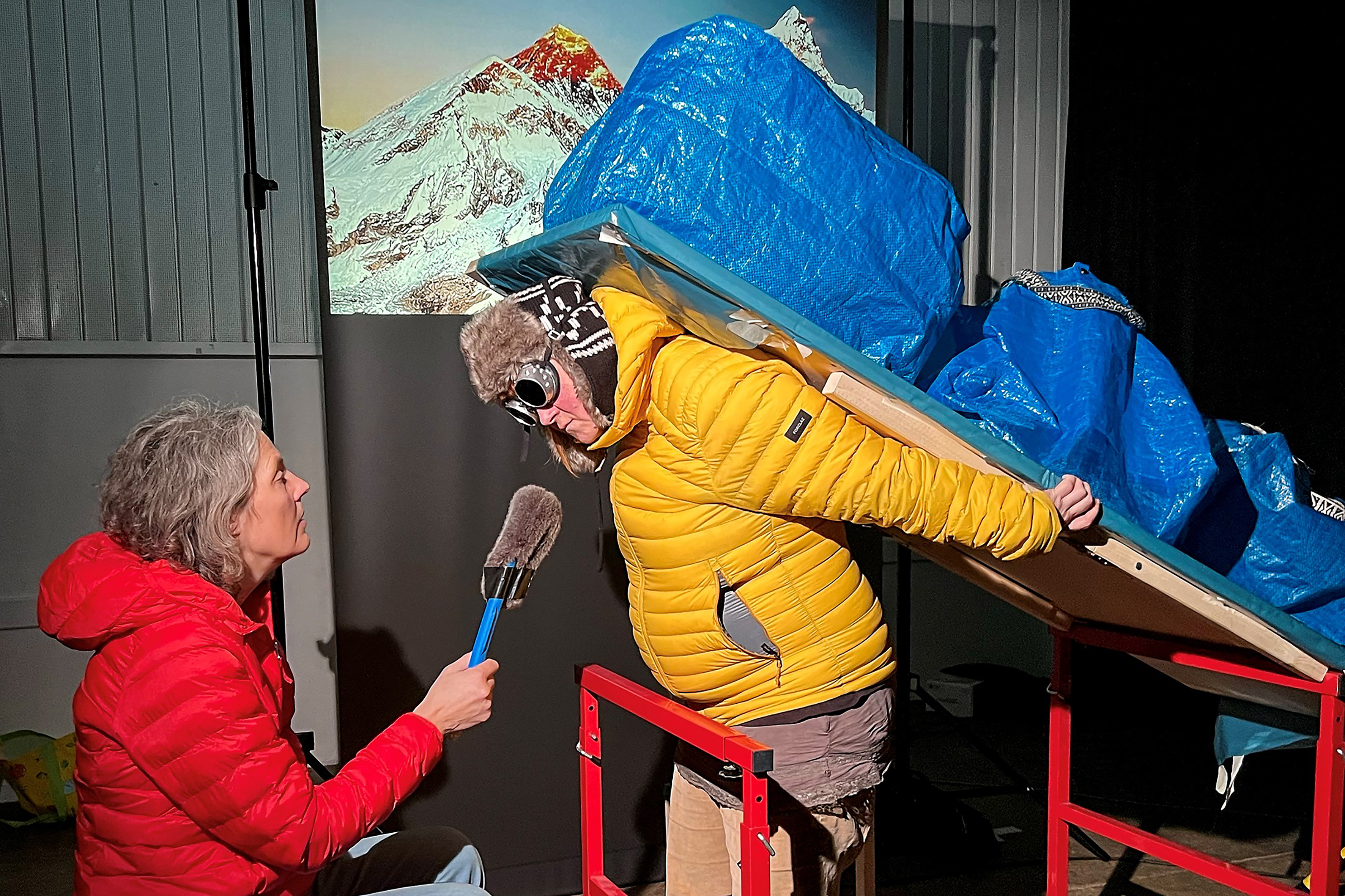 Puppenspielerin Eva Kaufmann interviewt die schwer bepackte Alexandra Kaufmann in dicken Winterklamotten. Im Hintergrund ist ein Bild des Mount Everest.