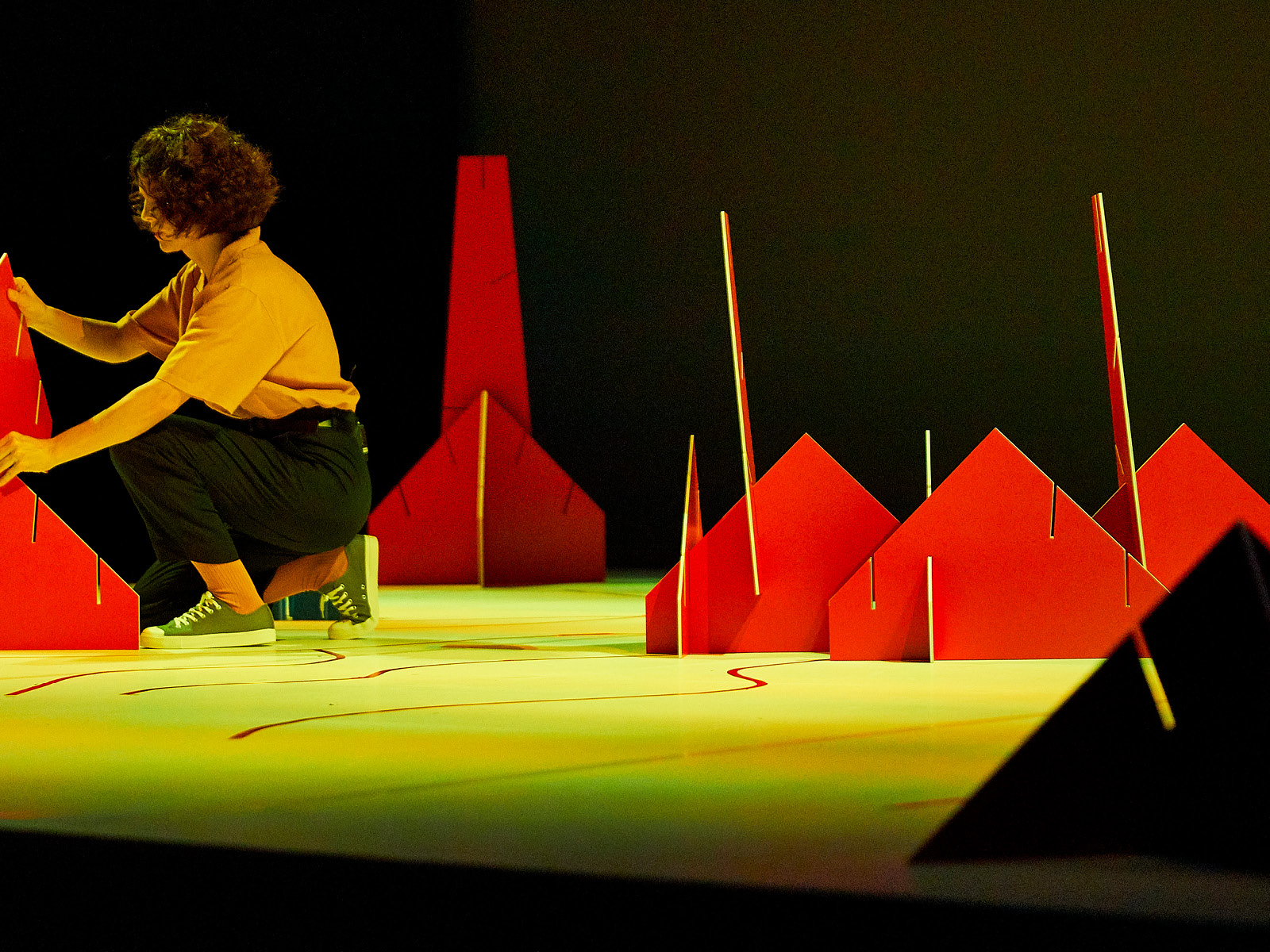 A woman kneels on the floor of a stage in the midst of patched-together, colorful surfaces.