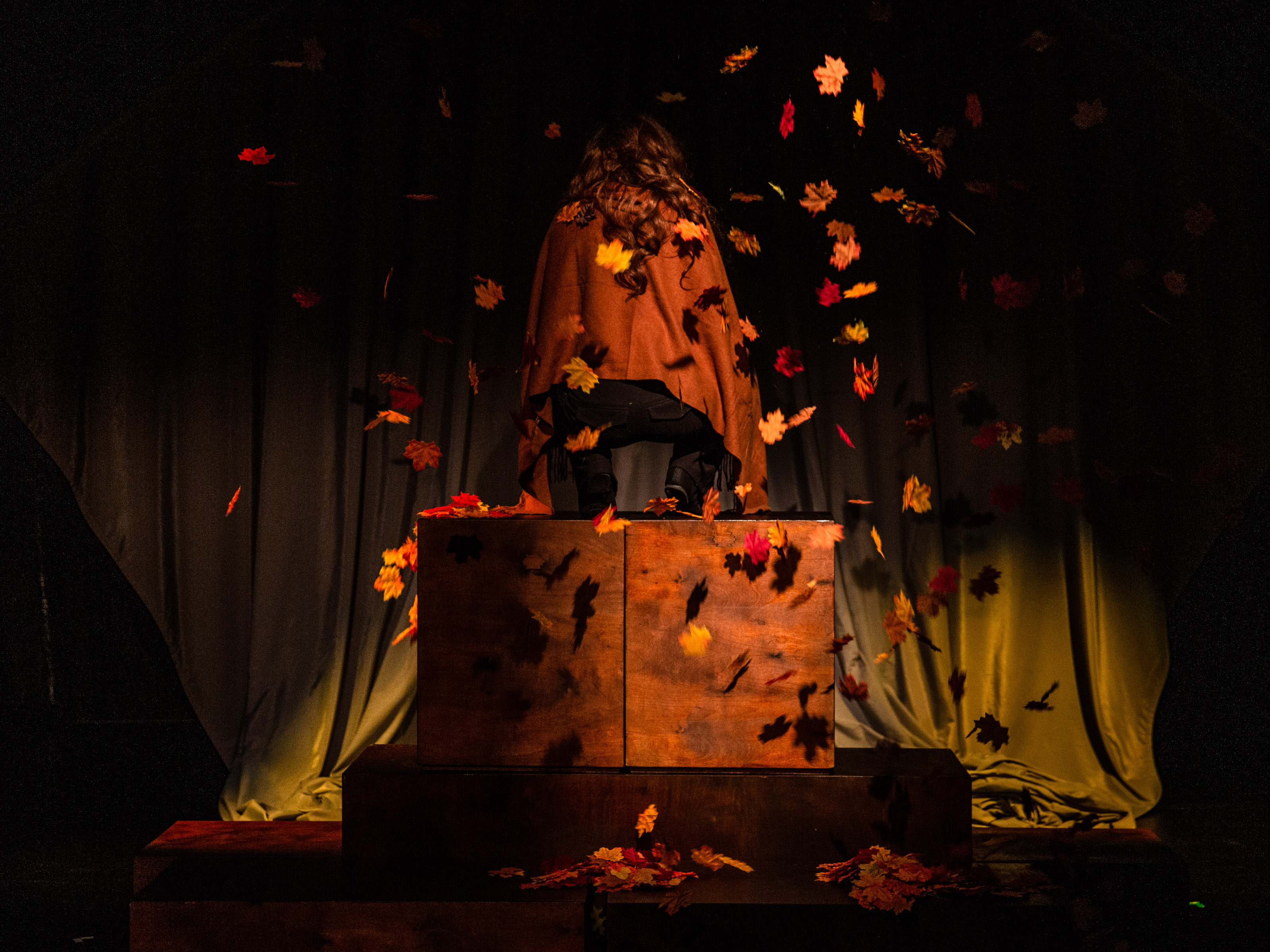 Helga's puppet has its back turned to the audience and kneels on a large wooden block. Autumn leaves rain down on her from the ceiling. She wears a brown cape in the same color as the leaves.