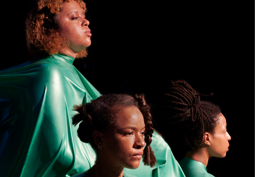 Three statuesque BPoC women are embedded in green latex and stare straight ahead.