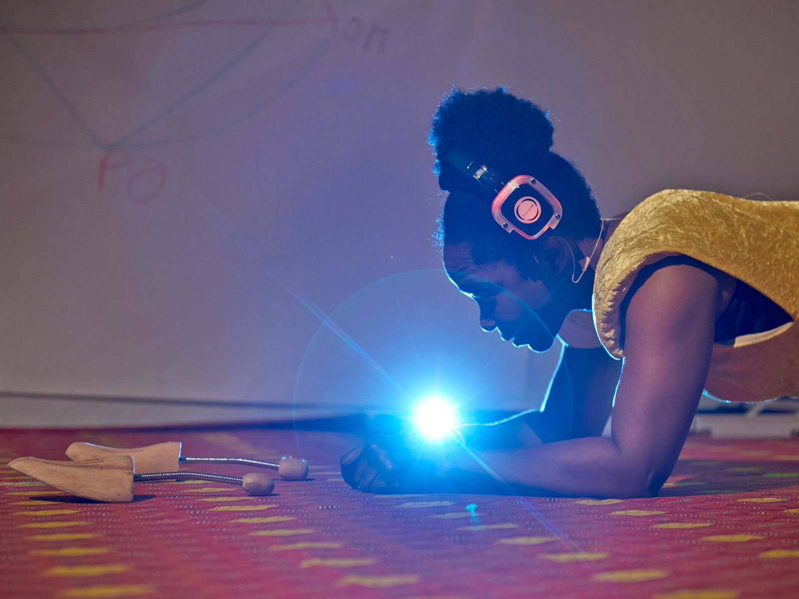 Eine der Spielerinnen stützt sich in Liegestützposition auf den Teppich. Sie trägt Kopfhörer und schaut in ein helles Licht zwischen ihren Händen.