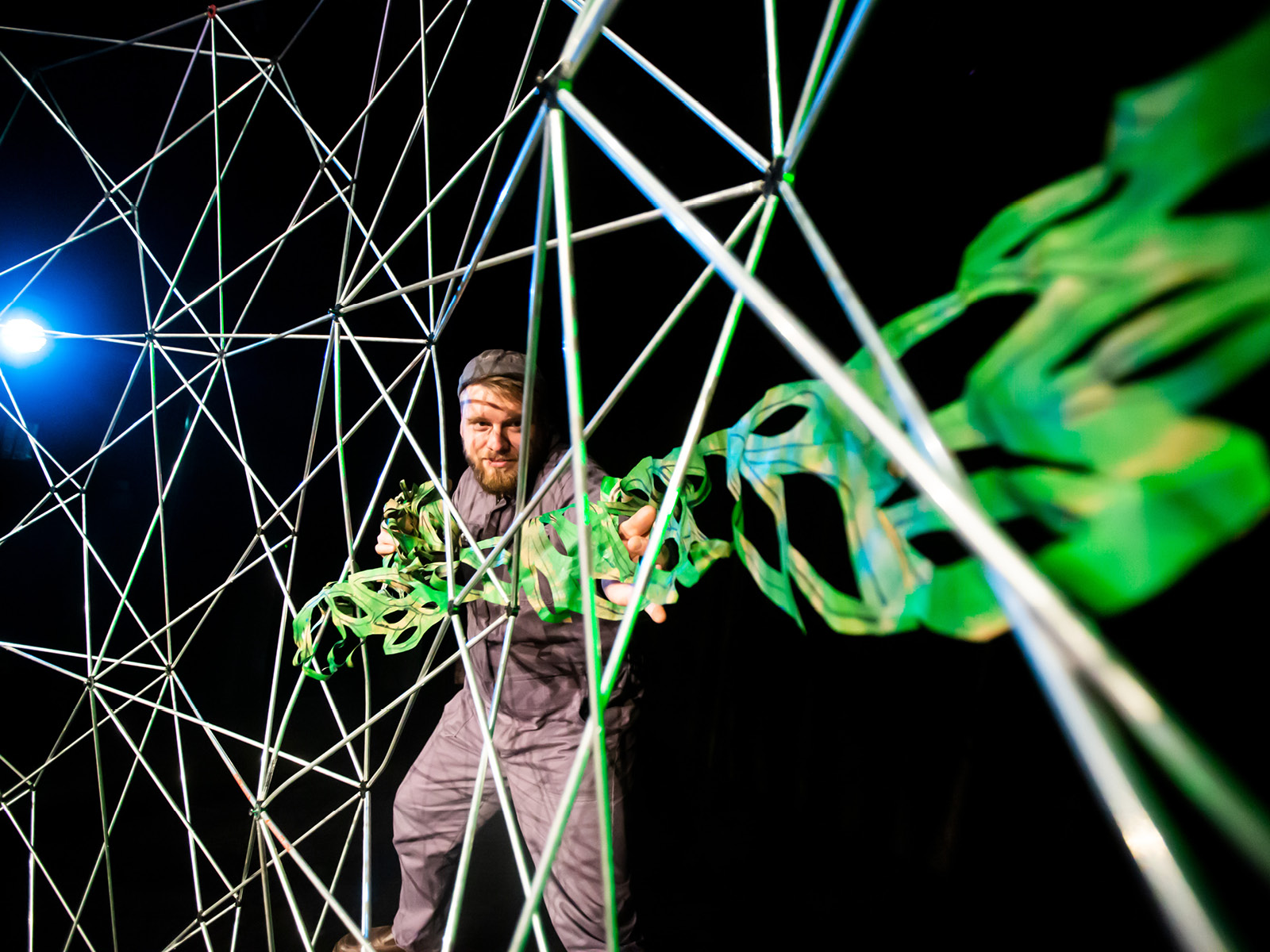 Eine lange, saftig grüne Pflanzenranke aus Papier bewächst das Metallgerüst im Hintergrund der Bühne, indem es von Artisane Stefan Spitzer hineingeschoben wird.