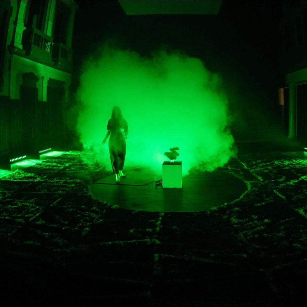 Eine Person läuft neben einer Maschine. Sie sind in dichten, grünen Nebel gehüllt.