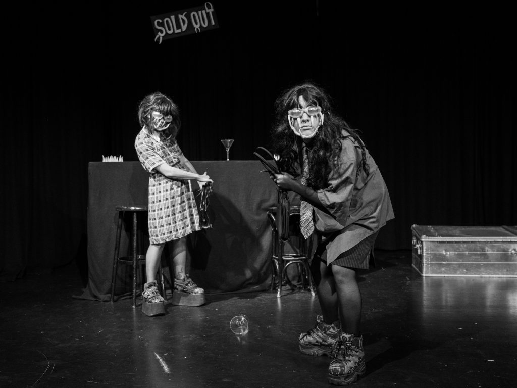 Zwei Personen mit Fangzahnbrillen stehen aufrecht und zusammengekauert in einer Bar.