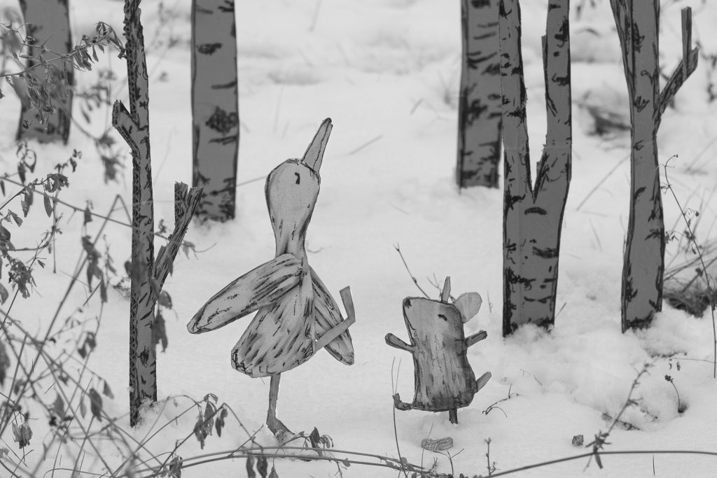 Die Pappfiguren einer Gans und einer Maus laufen durch eine Schneelandschaft
