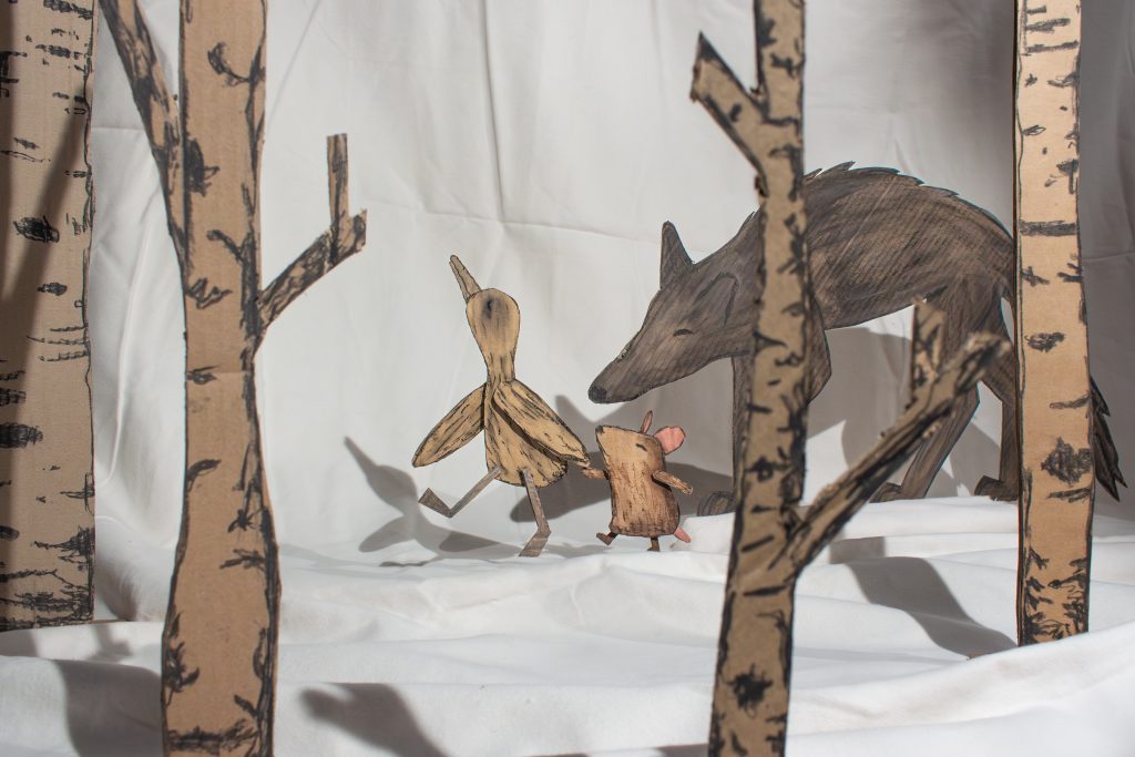 Die Pappfiguren eines Wolfes, einer Gans und einer Maus laufen durch eine Schneelandschaft