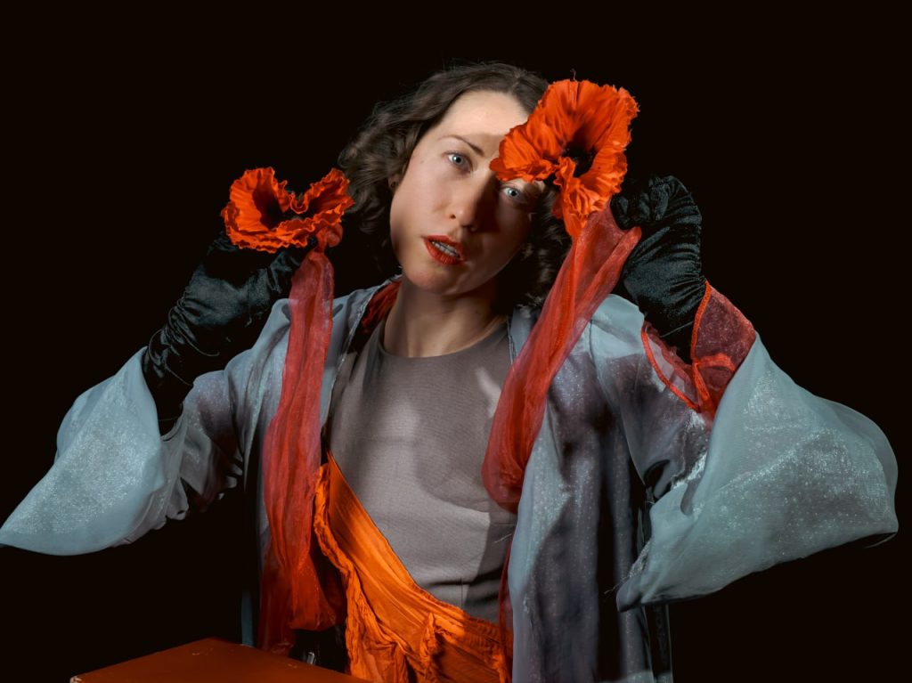 Eine junge Frau hält sich theatral zwei orangene Stoffschleifen vors Gesicht