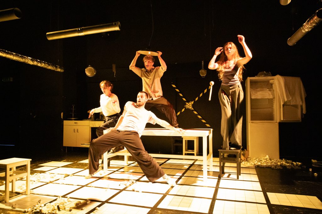 Vier Personen stehen dynamisch verteilt in einer Küche.