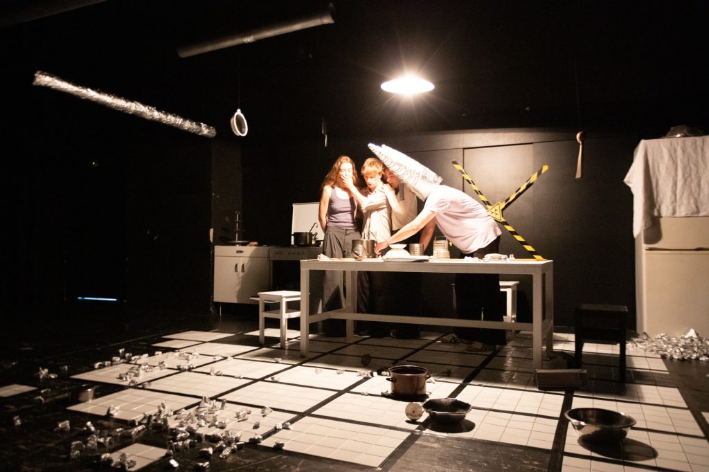 Verschiedene Personen stehen in einem Küchenraum. Sie tragen teilweise Kostümteile.