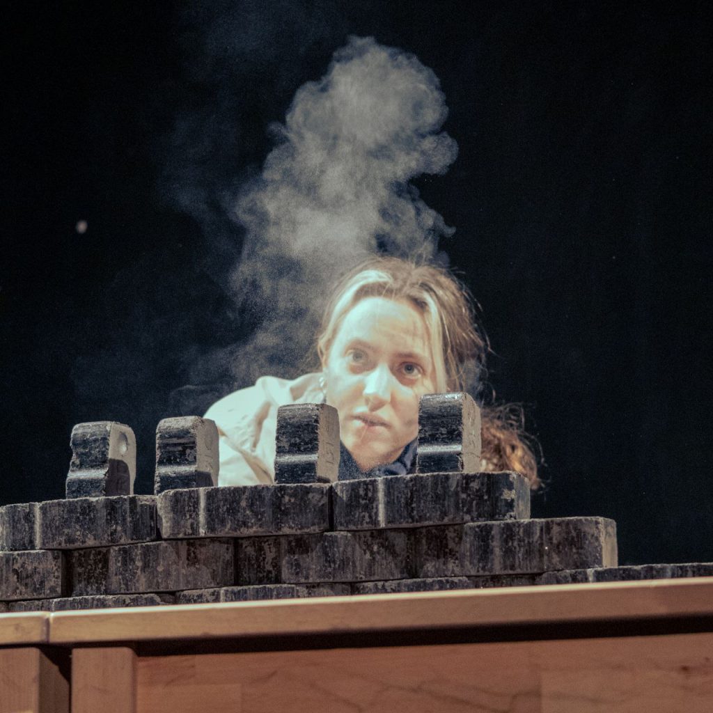 Eine junge Frau steht hinter einem Holzmöbel. Vor ihr tritt Rauch aus.