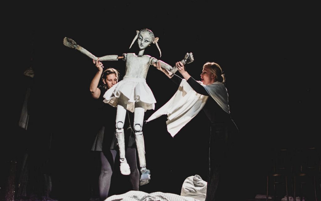 The picture shows two puppeteers and a life-size puppet. The puppeteers are holding the puppet in the air, making it look as if it is jumping up.