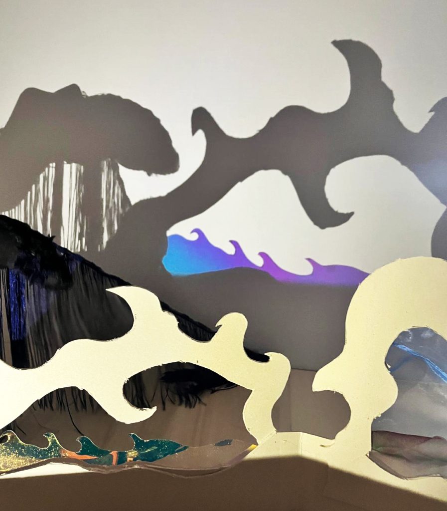 Abstrakte wellenartige Scherenschnittformen in Beige werfen Schatten in Schwarz und Violett vor hellem Hintergrund.