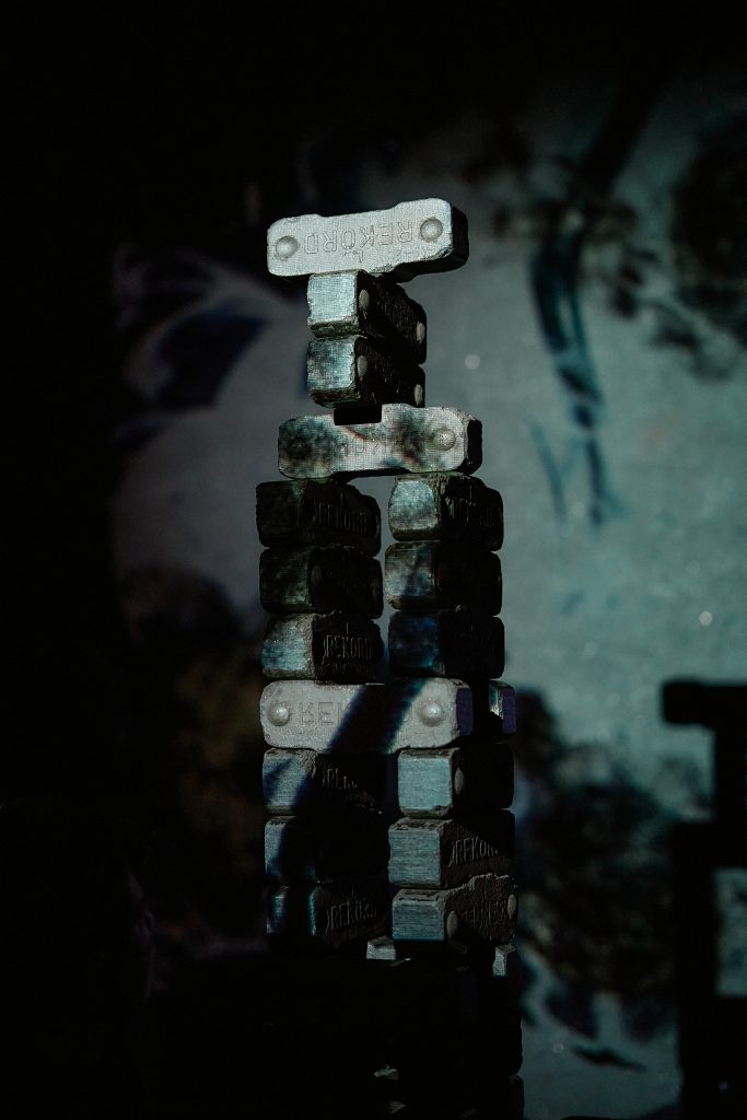 A vertical structure made of several dark rectangular blocks is stacked and connected by lighter components. The scene is dimly lit, causing the construction to stand out against a dark background.