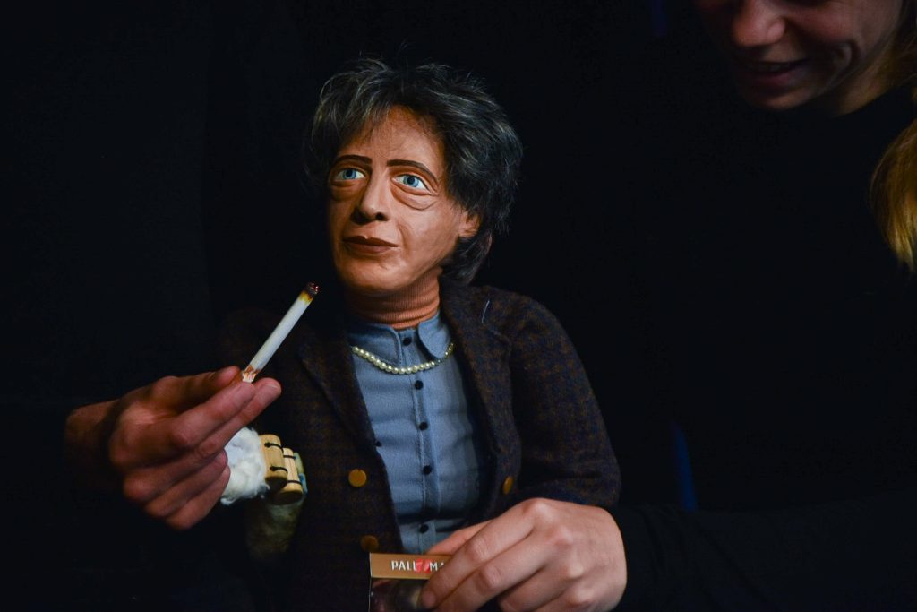 Eine Puppe, die Hannah Arendt darstellt, nimmt eine Zigarette.