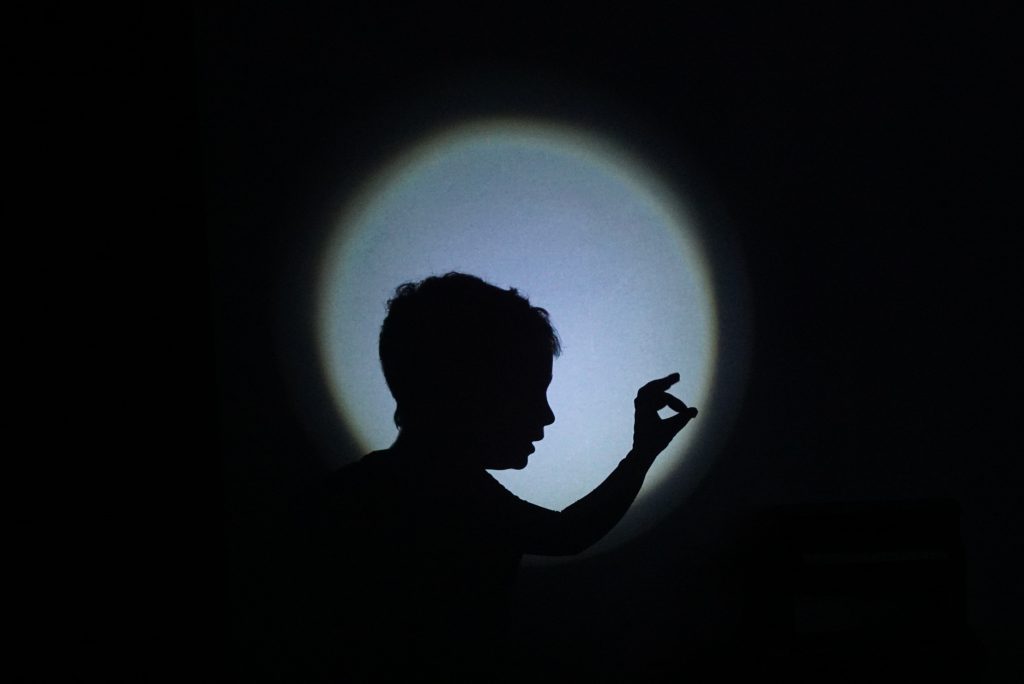 Silhouette einer Person vor einem Lichtkreis, die mit den Fingern eine Form bildet.