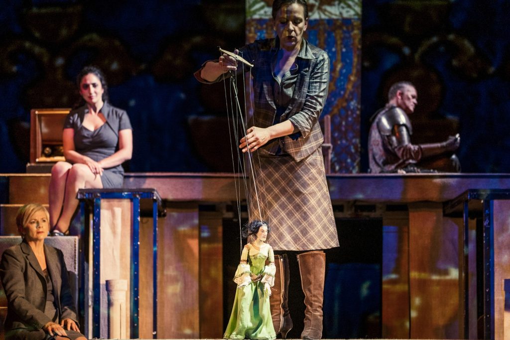 Marionette im grünen Kleid wird von einer Person auf einer Theaterbühne geführt.