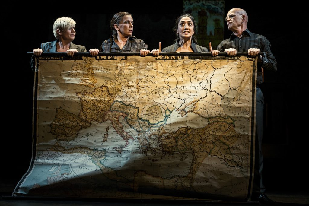 Four performers hold a large map used as a stage backdrop.