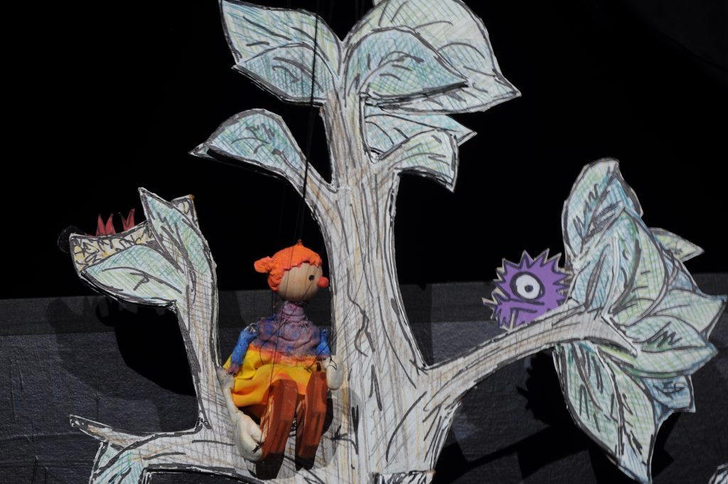 Puppet nestled among the branches of an illustrated tree.
